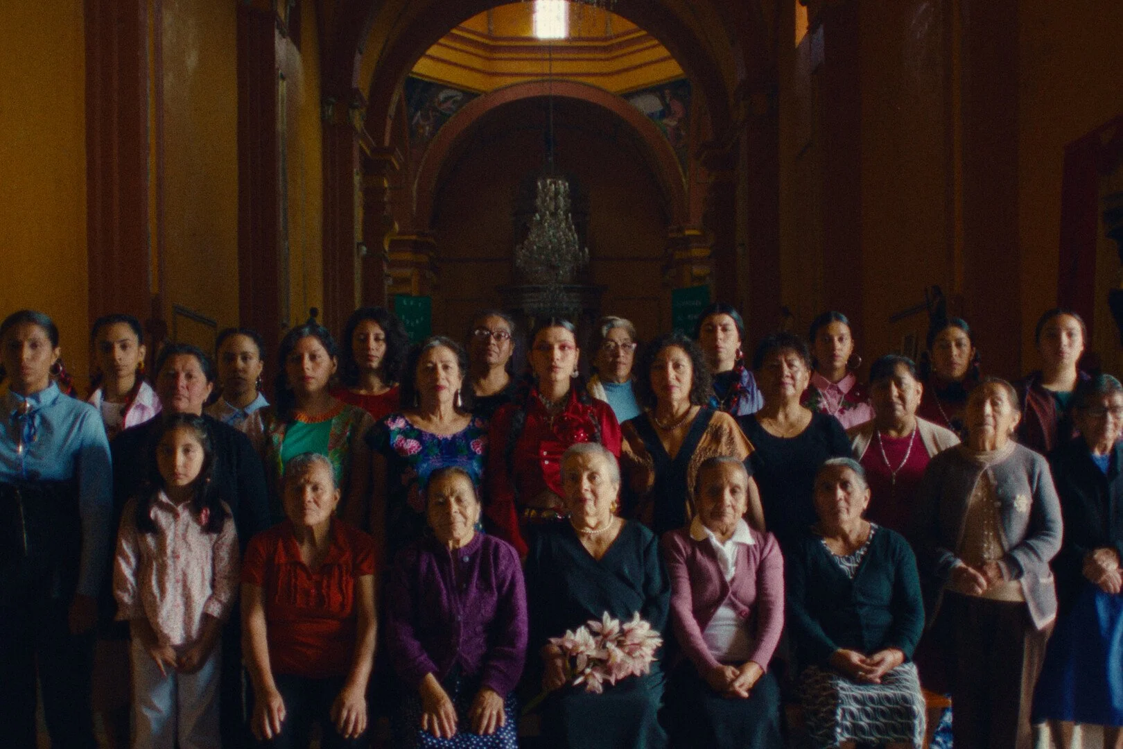 The artist dressed in bright reds, standing amongst older Mexican women in a church.