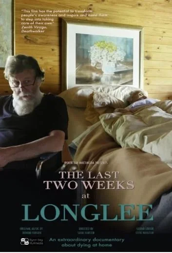 A man with glasses and a beard sitting in a chair next to an elderly woman lying in bed. The room has wood-paneled walls and a framed floral painting behind the bed. The image features text promoting a documentary titled "The Last Two Weeks at Longle