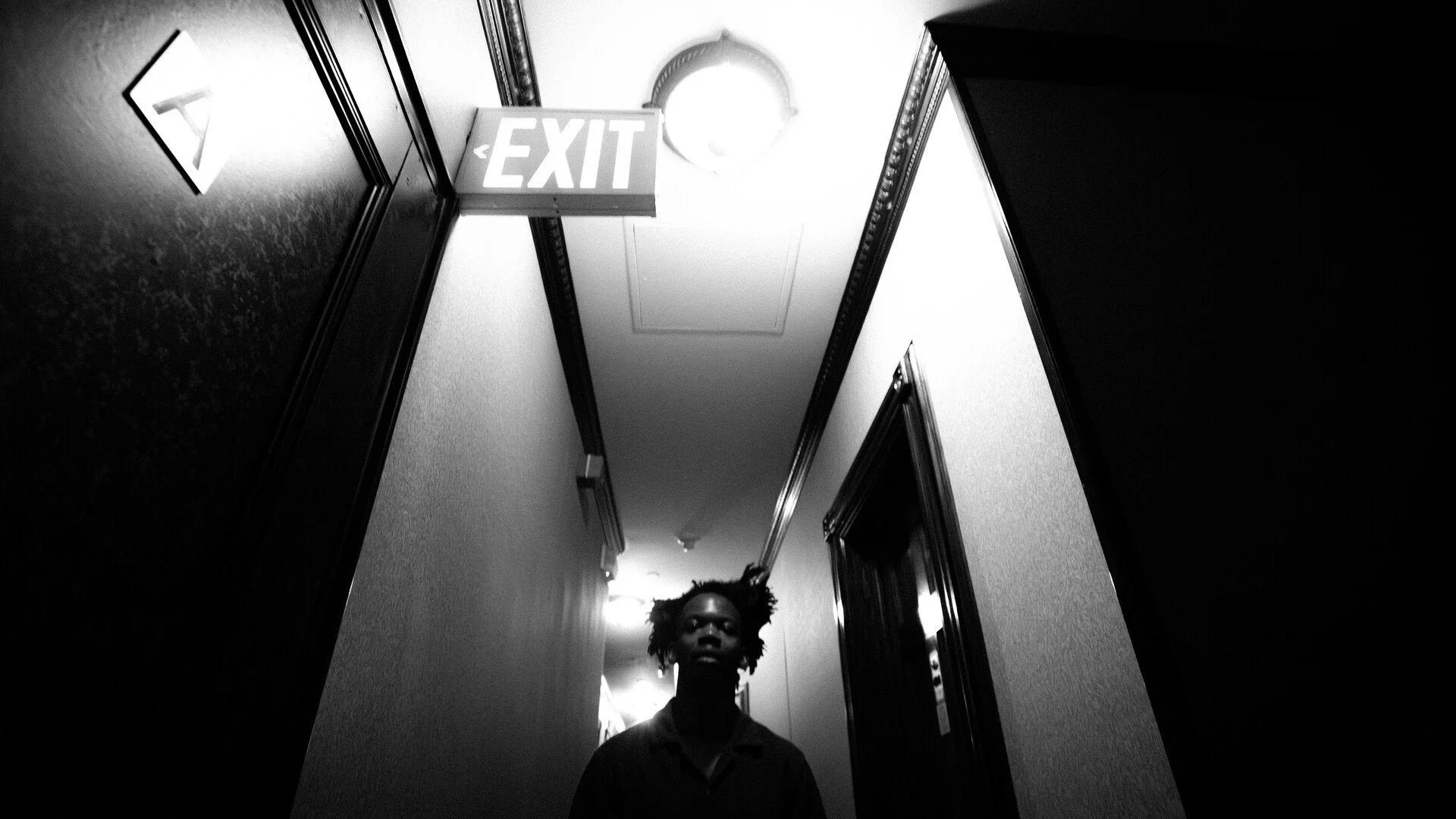 A man standing in a hotel hallway with a big 'EXIT' sign.
