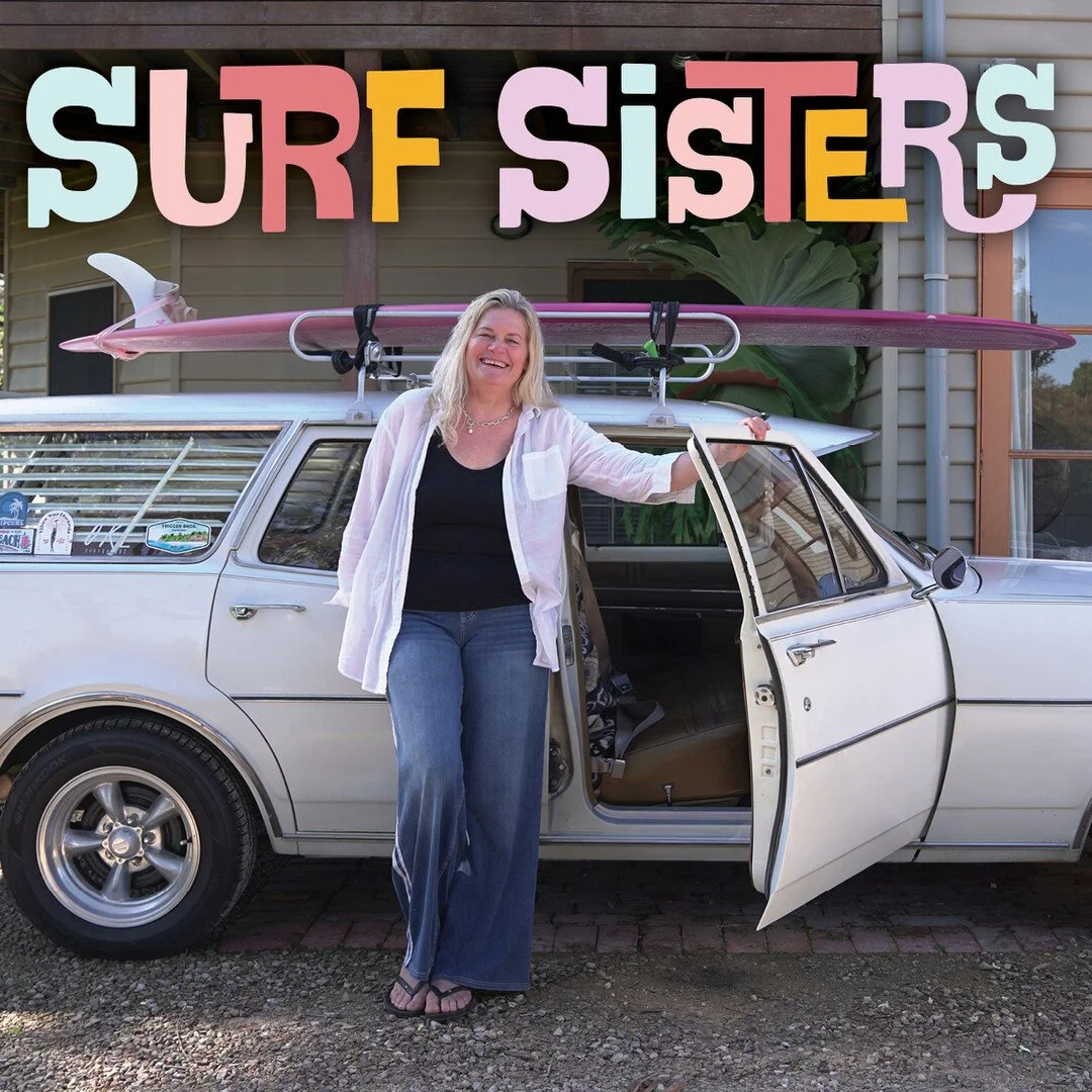 Poster for Surf Sisters. A smiling woman stands beside an open car door of a white vintage station wagon with a pink surfboard strapped to the roof rack, parked in a driveway. Playful, multicoloured hand-drawn title lettering appears above her.
