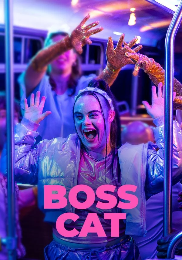 Movie poster for Boss Cat. A young woman with Down syndrome stands on a bus, laughing with arms raised, wearing a silver jacket, lit in vivid purple and pink nightclub lighting. Title in bold pink block letters.