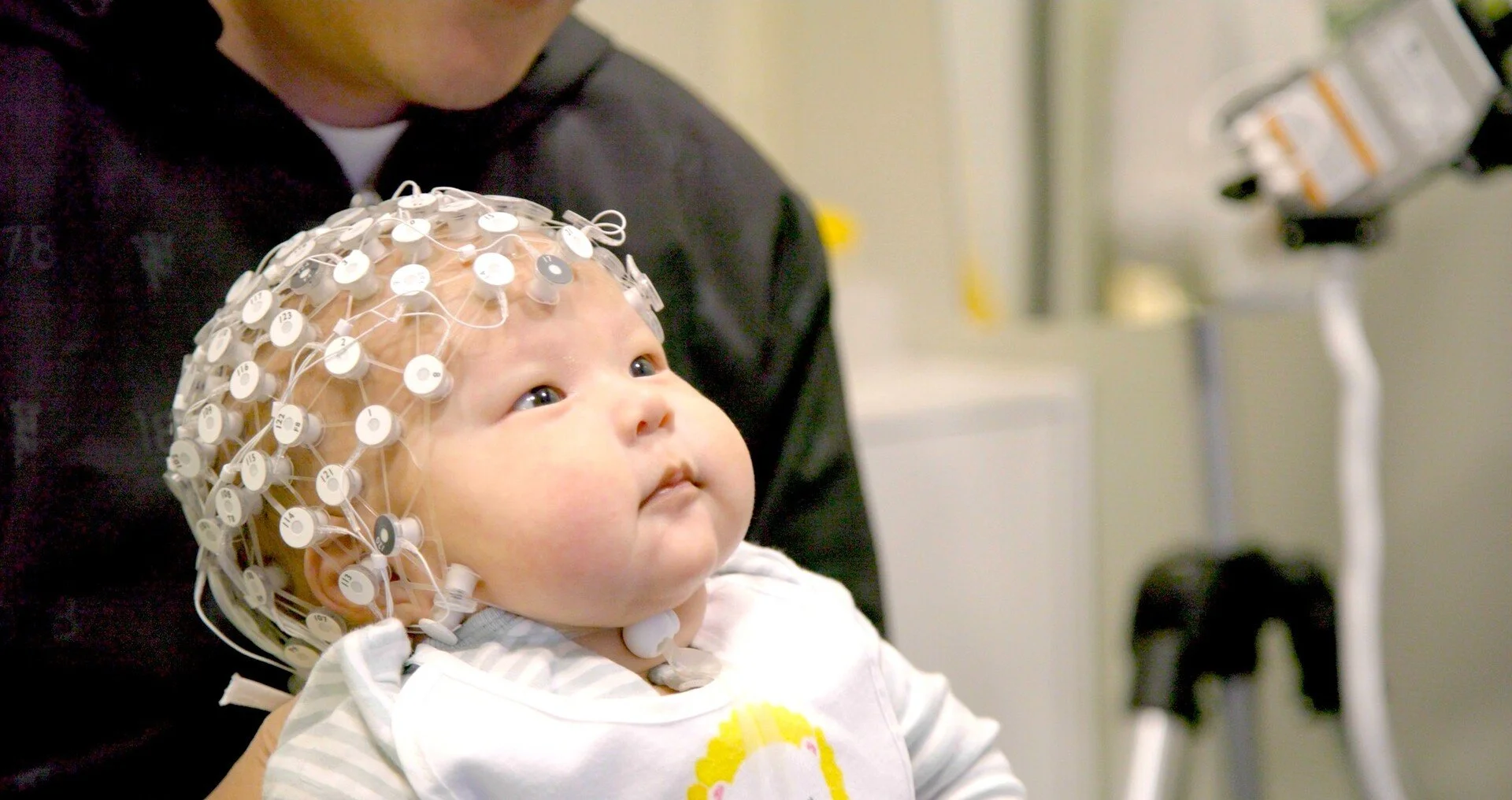 Still image from the film "Raising Superheroes" showing a baby with a brain scanning machine attached to their head