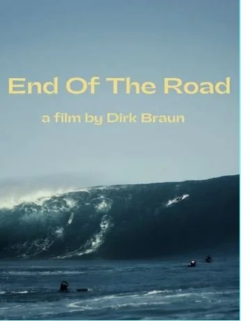 Surfers in dark water face a massive, approaching wave under a cloudy sky. Text reads "End Of The Road, a film by Dirk Braun," conveying an adventurous tone.