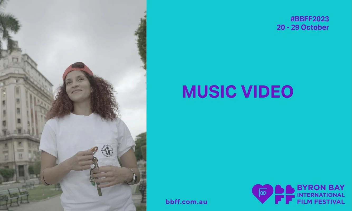 Young person with curly hair, wearing a red cap and white t-shirt, stands outdoors. The text promotes the Byron Bay International Film Festival 2023.