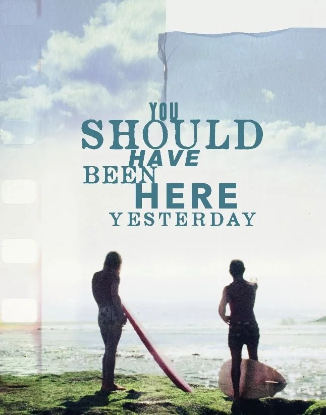 Two surfers stand on a grassy cliff, gazing at the ocean under a cloudy sky. Text overlays: "You should have been here yesterday."