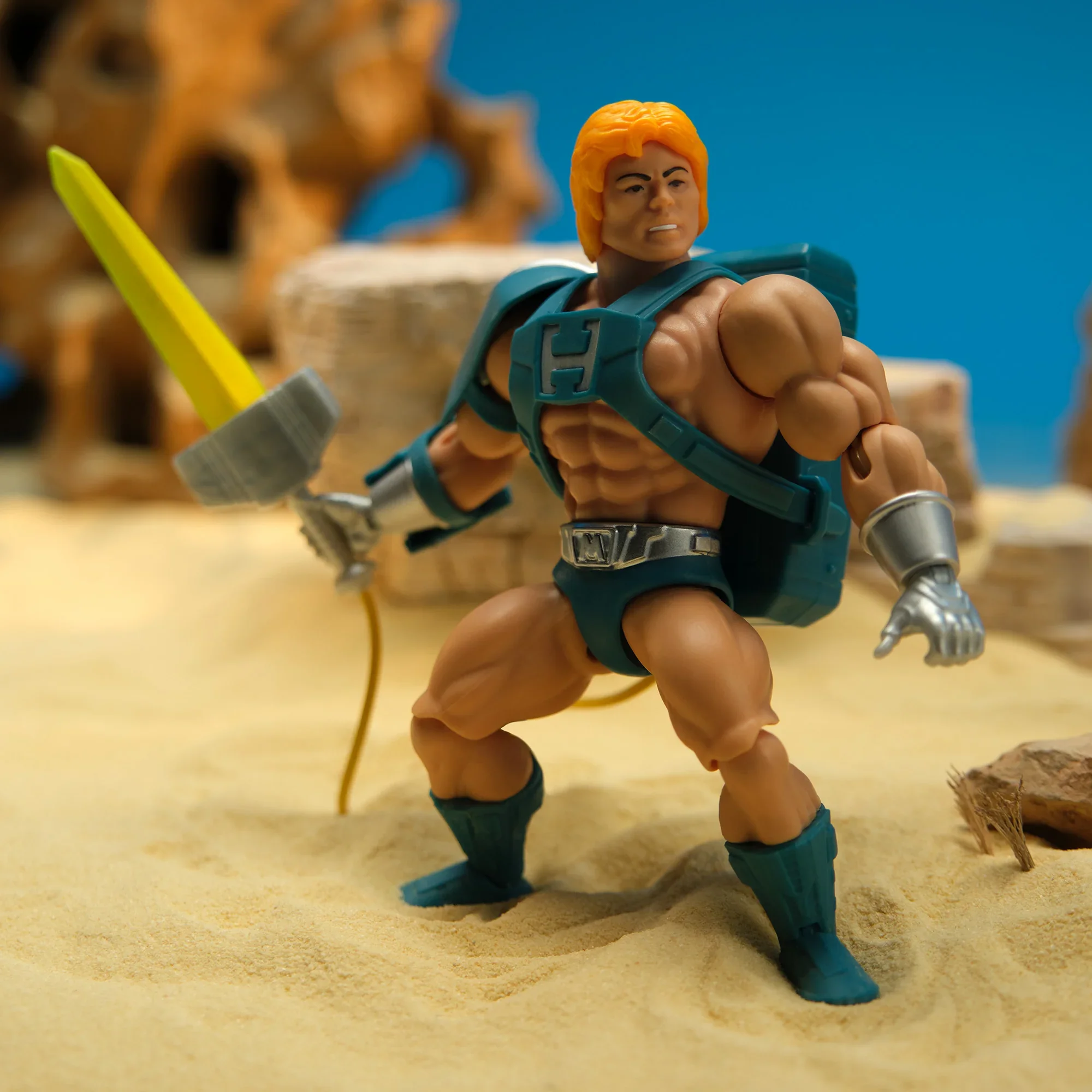 Mattel MOTU Origins Deluxe Laser Power He-Man action figure in dynamic battle pose holding the light-up green Power Sword, displayed in desert landscape scene.