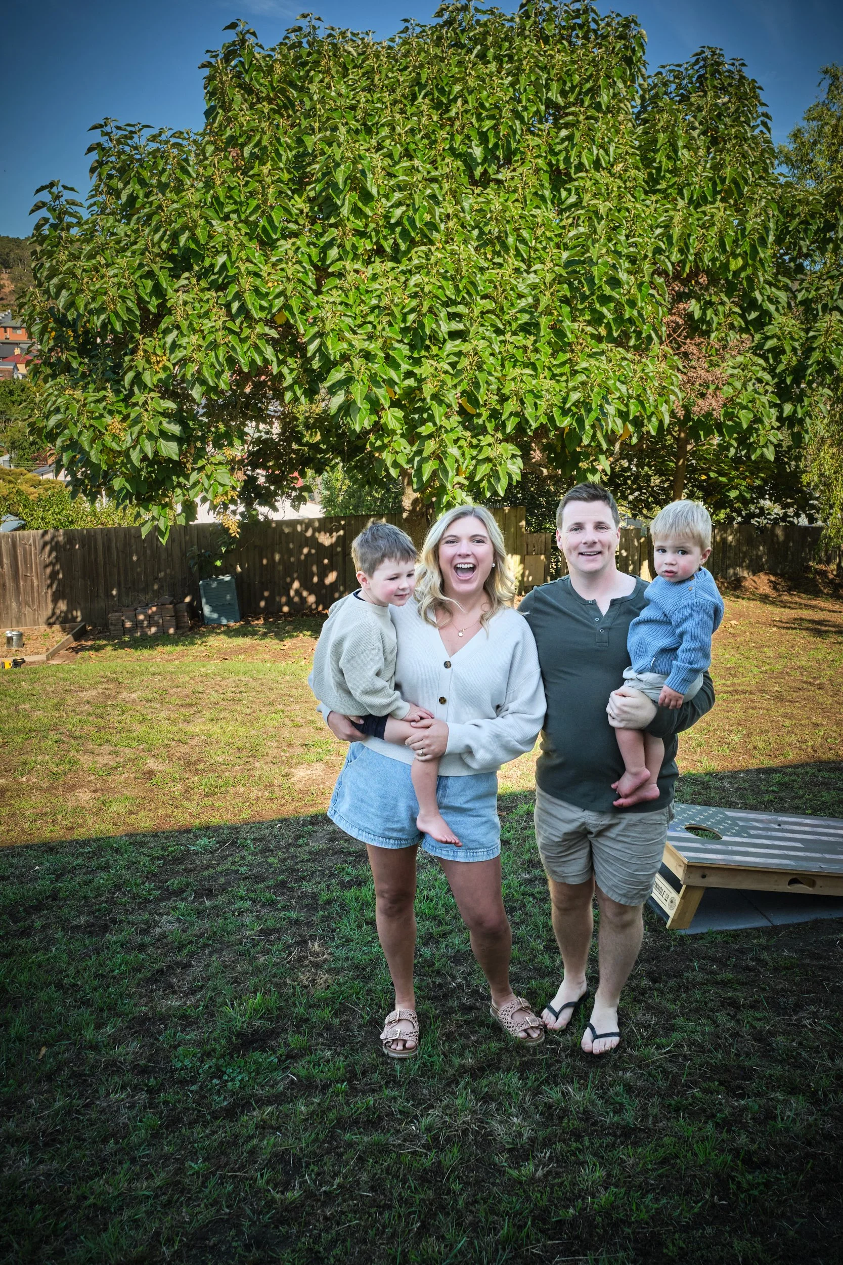 macdonald-launceston-family-portrait-parents-holding-two-children-backyard-tree.jpeg