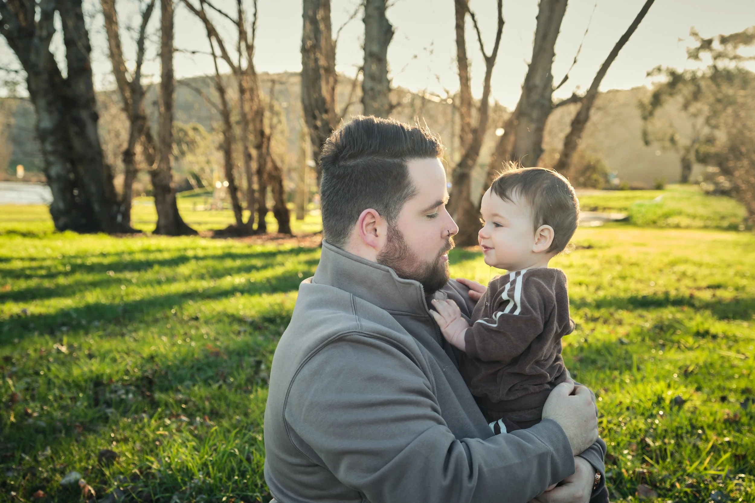 williams-hadspen-river-launceston-family-portrait-father-holding-baby-in-sunny-park.jpeg