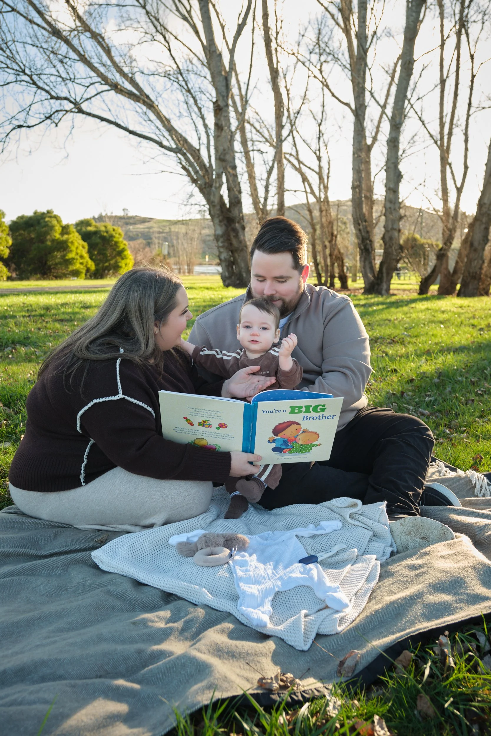 williams-hadspen-river-launceston-family-portrait-session-parents-reading-to-baby-outdoors.jpeg