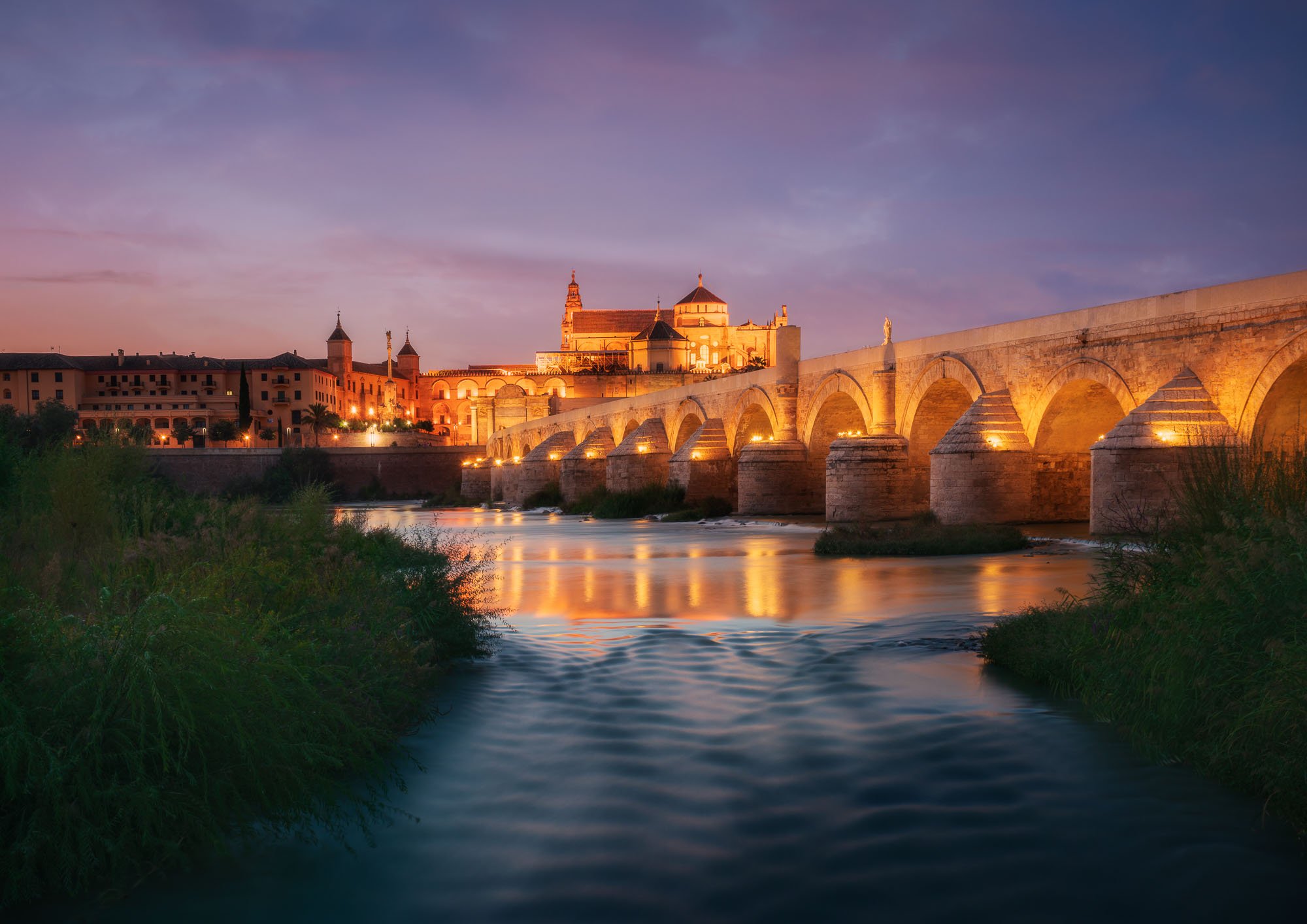Cordoba at twilight with historic bridge and river—soft reflections and sunset color.
