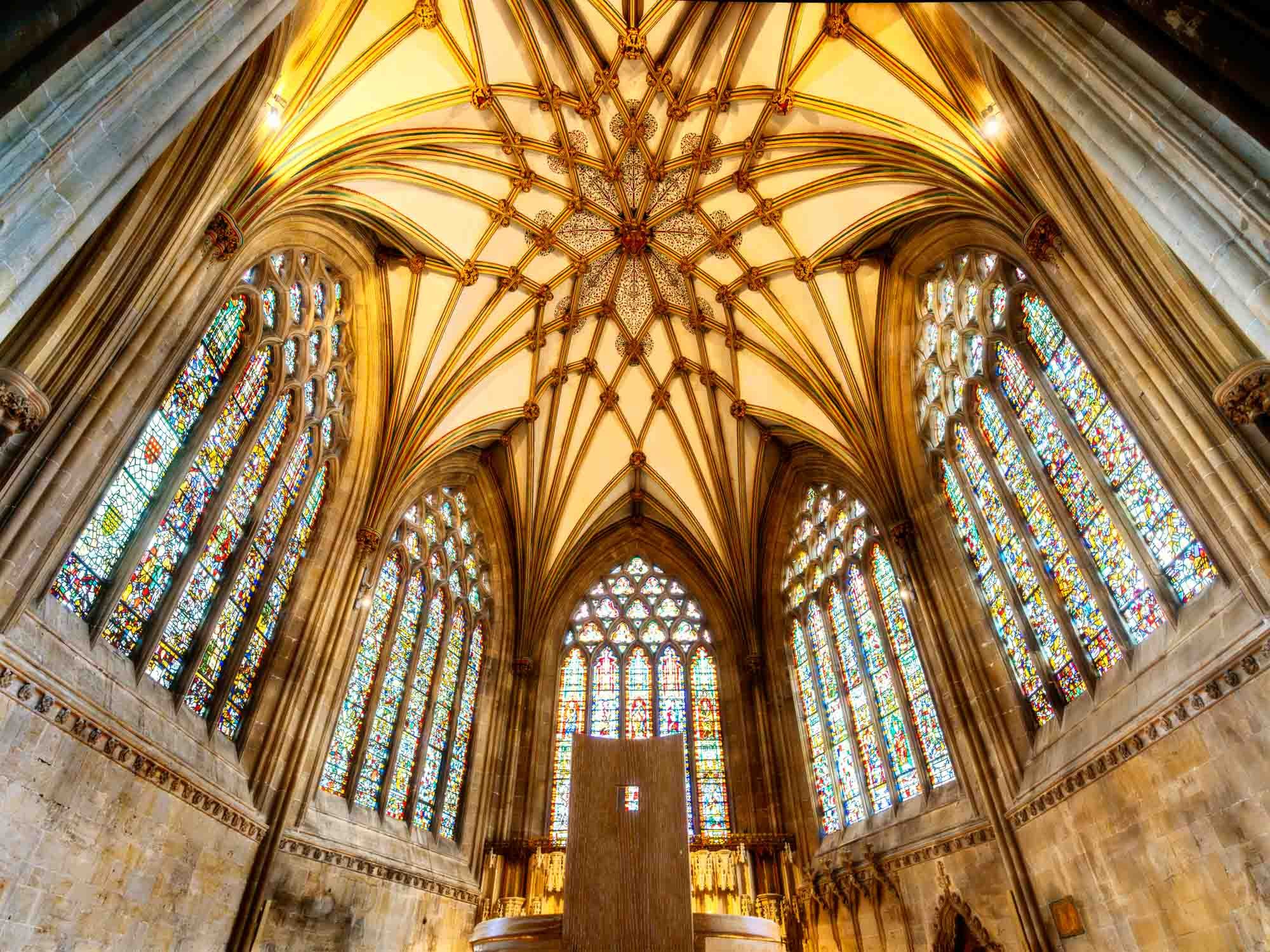 Golden stained glass and ornate ceiling in the Chapter House at Wells Cathedral