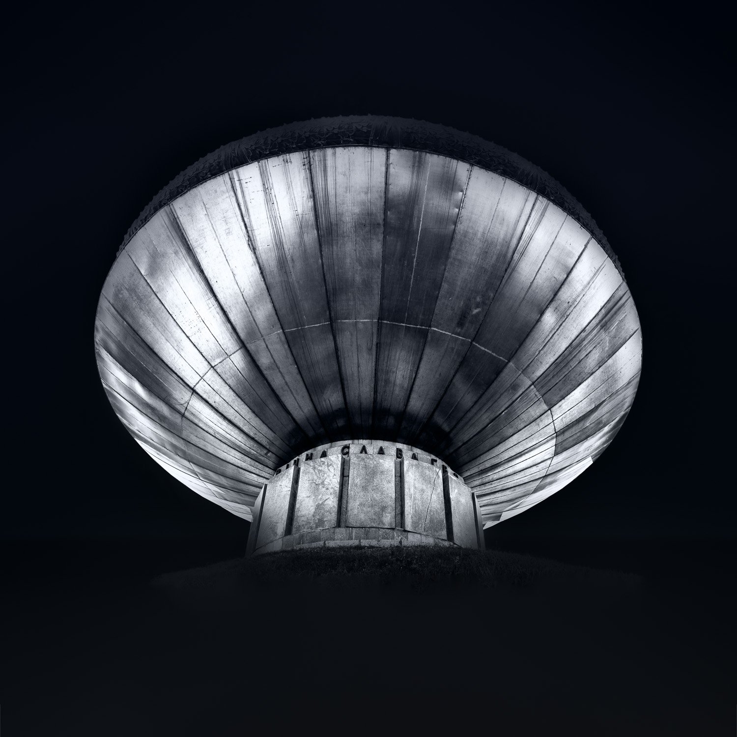 Black and white fine art photograph of a monumental, metallic war memorial rising from darkness, with the inscription 'Glory to the Heroes' in Cyrillic.