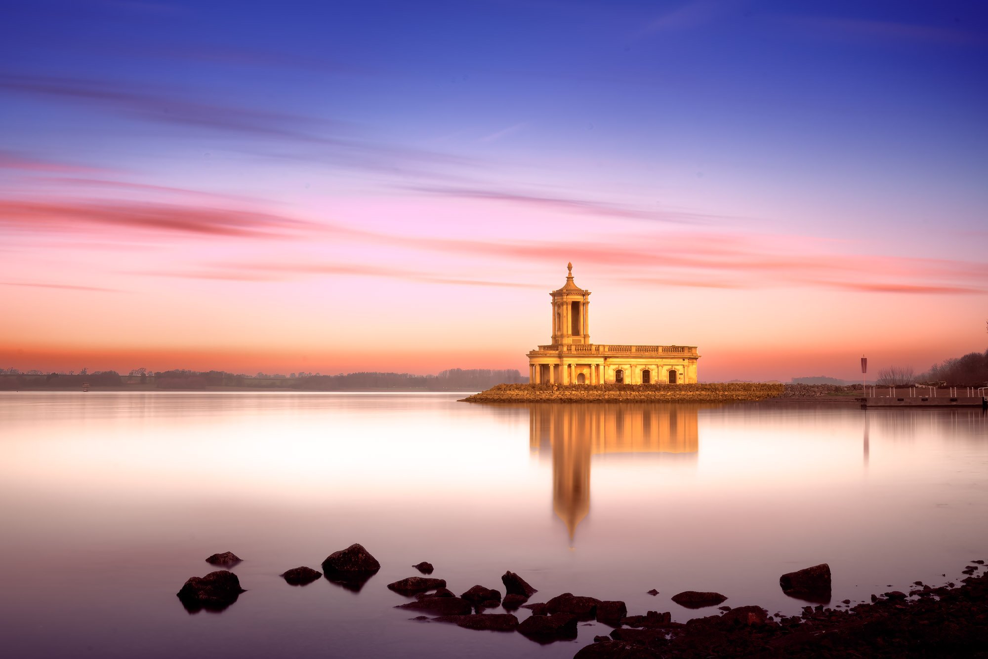 Normanton Church under a violet-pink sky during sunrise with still reflections