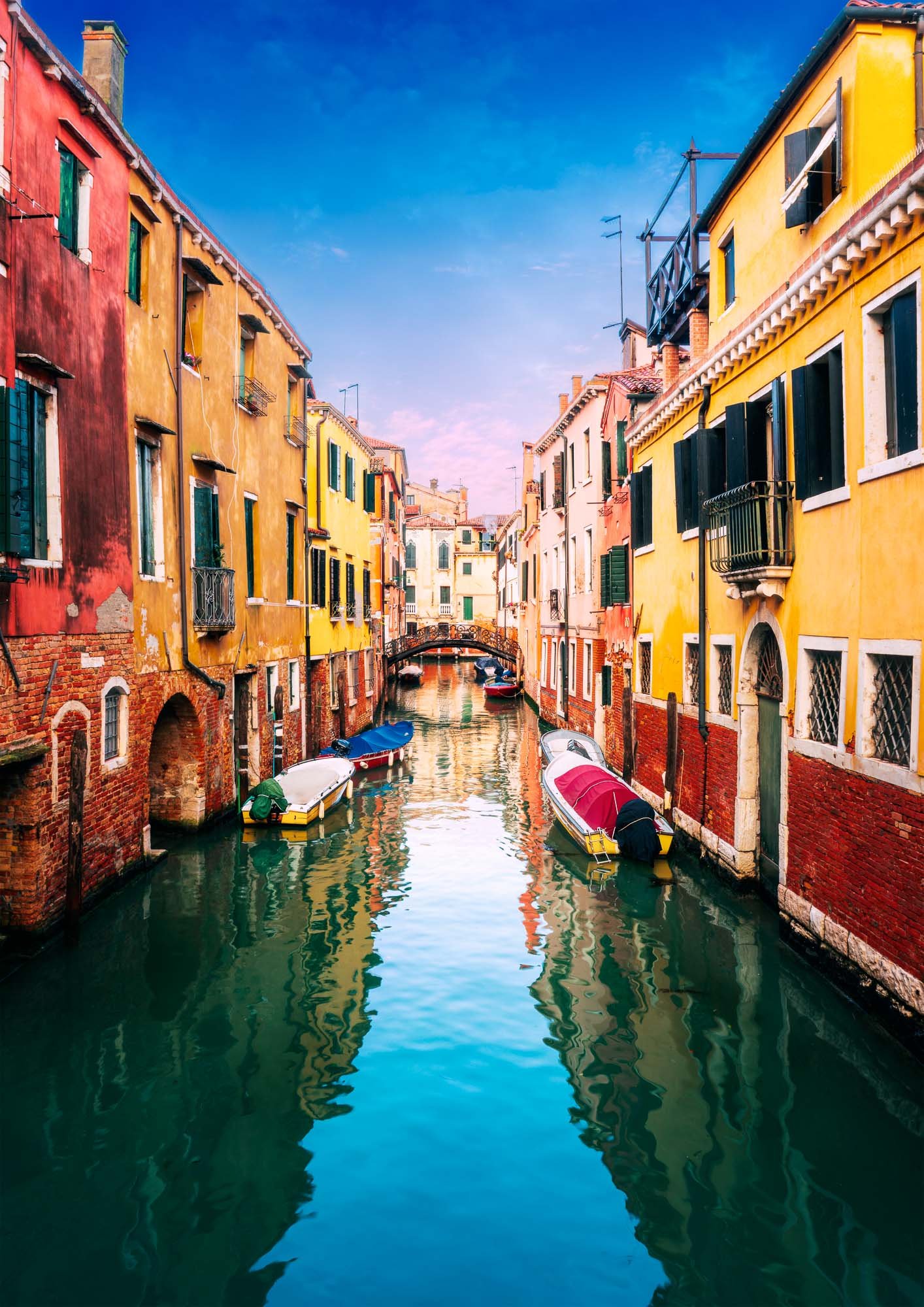 Colorful Venetian canal with boats, historic buildings, and reflections in the water under a pastel sky