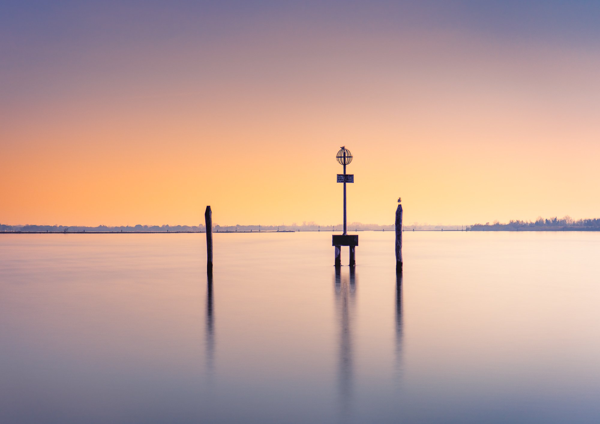 Venetian lagoon at sunset—pastel colors and gondola poles mirrored in still water.