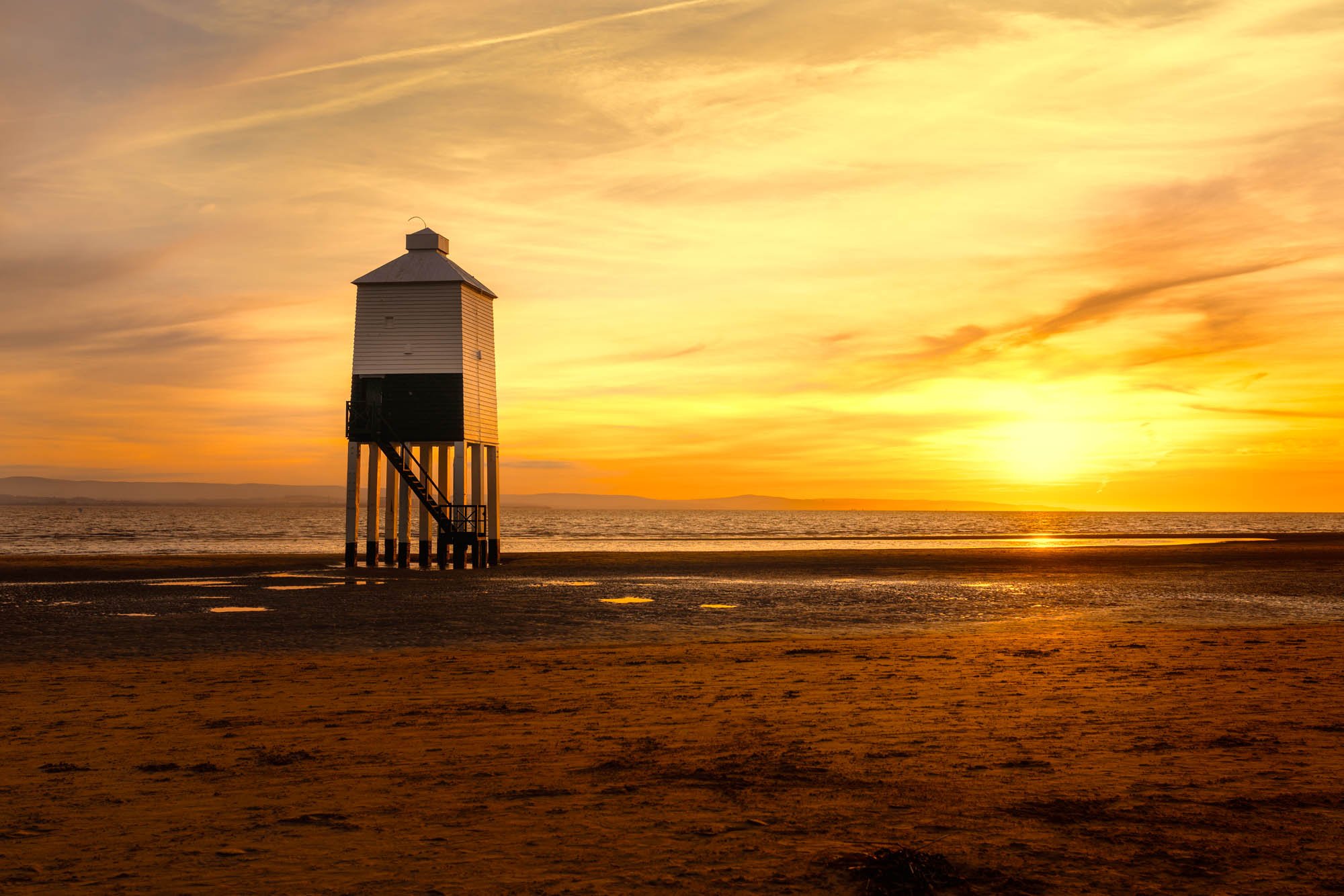 Golden hour tones illuminate Burnham lighthouse against the sandy beach
