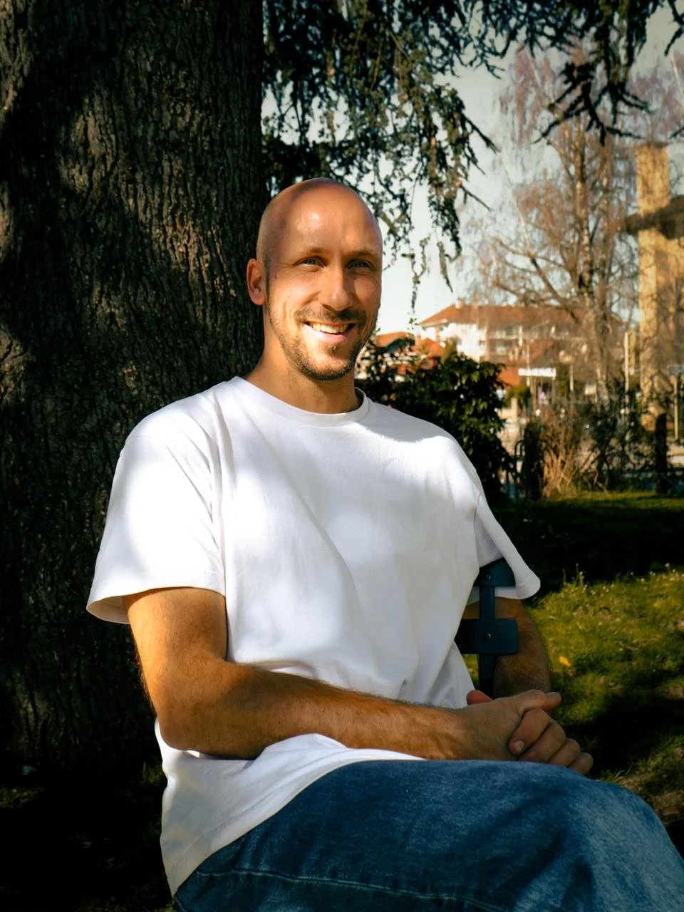 Un homme souriant assis sous un arbre dans un parc ensoleillé.