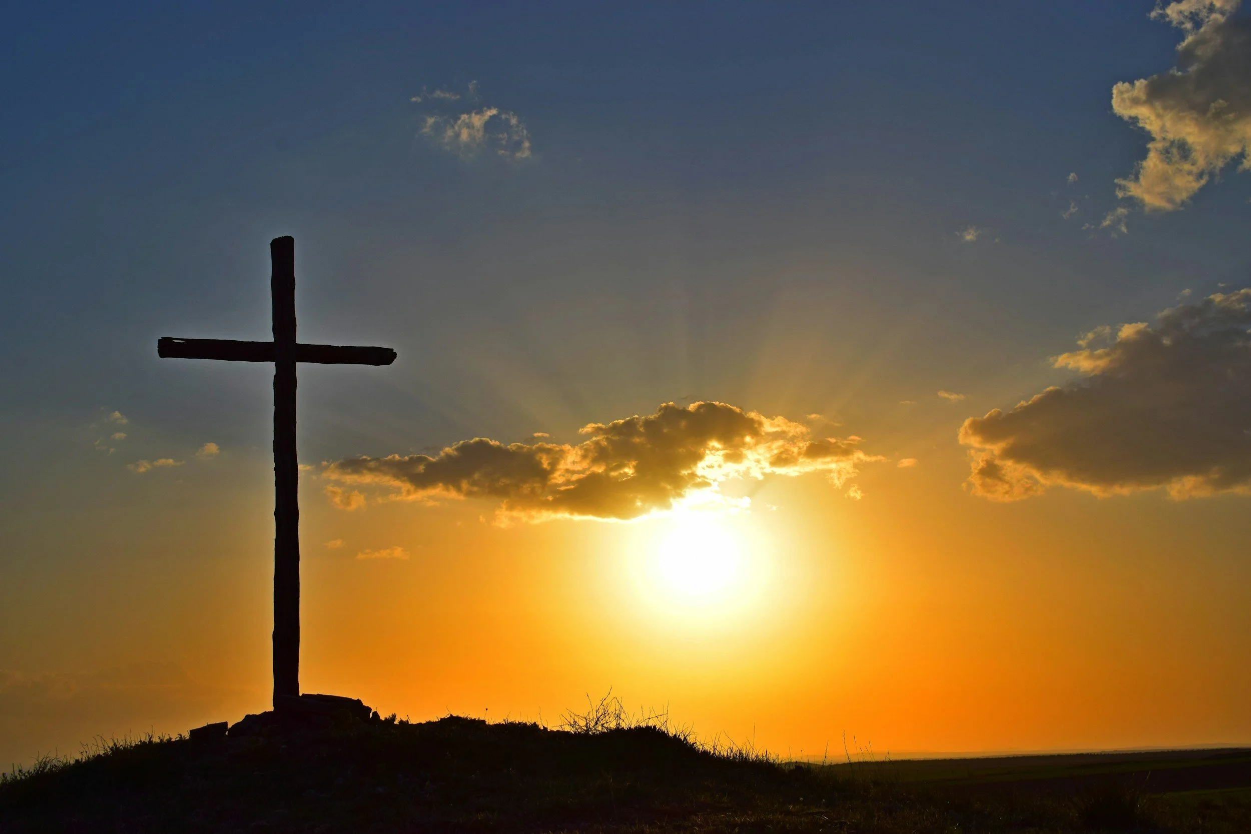 An empty cross on a hillside, lit by the rising sun.