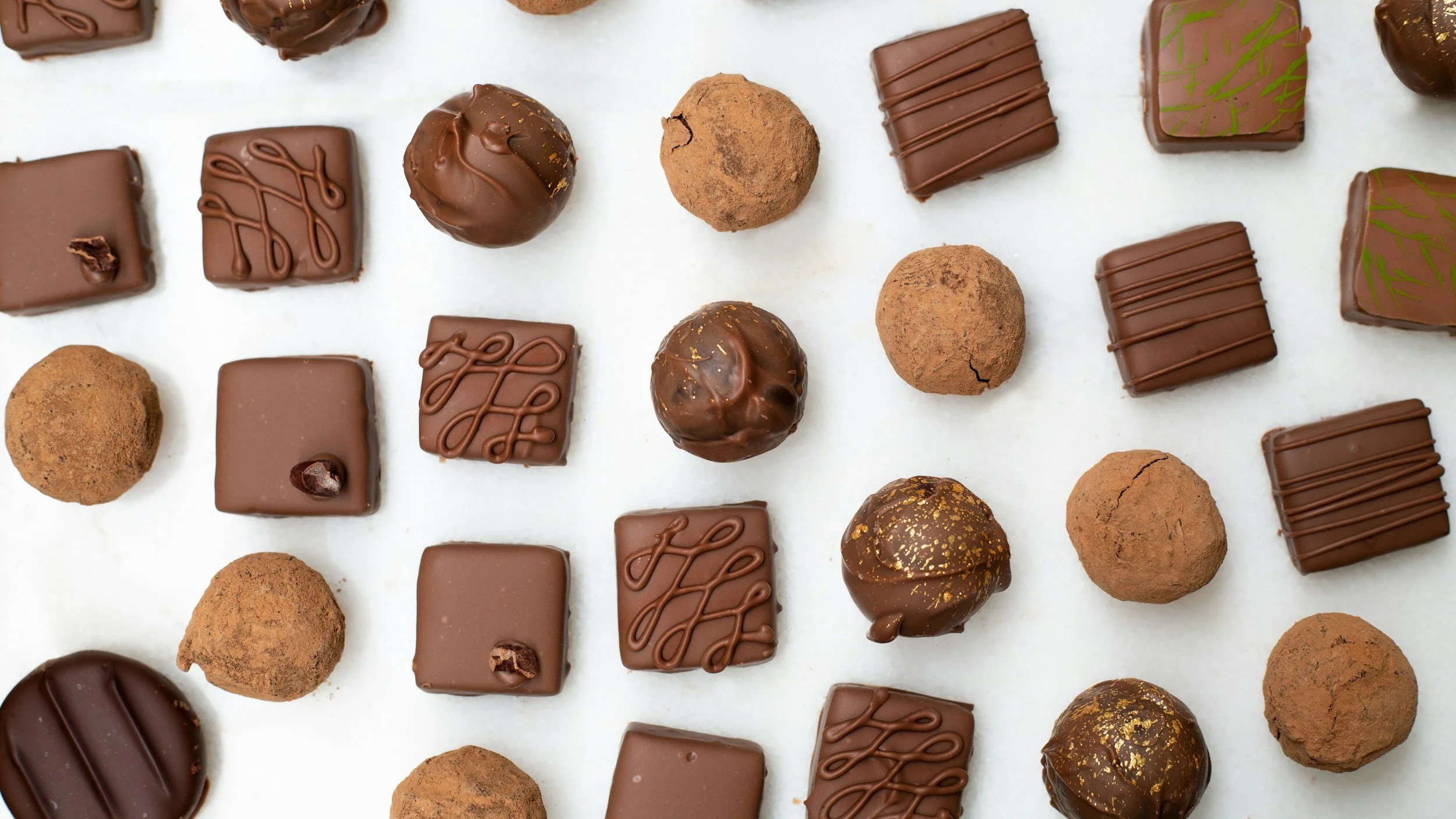 A selection of individual chocolate truffles, laid out in a diagonal pattern.