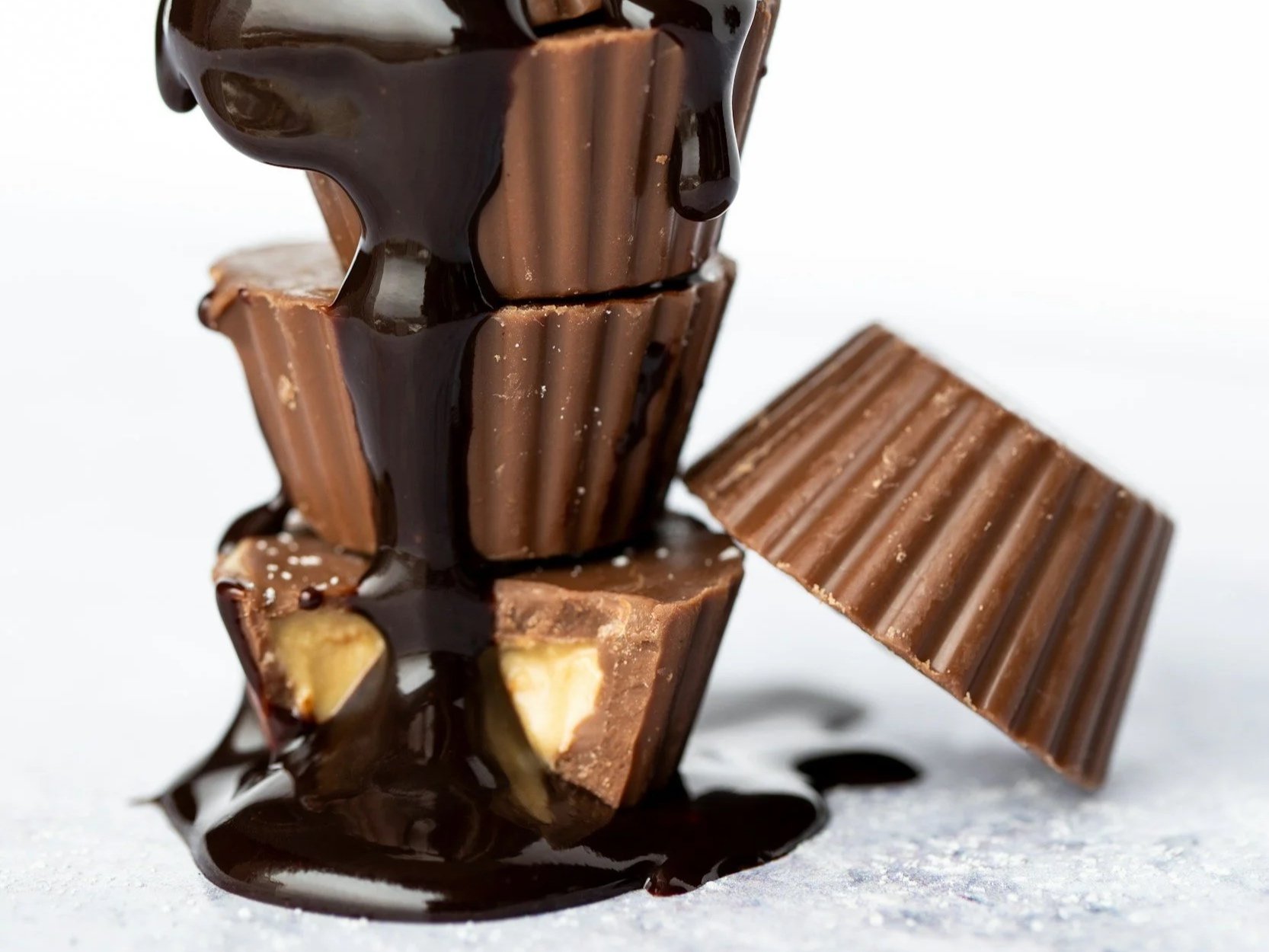 A stack of chocolate cups, some revealing light cream interiors, is beginning to be covered by molten dark chocolate.