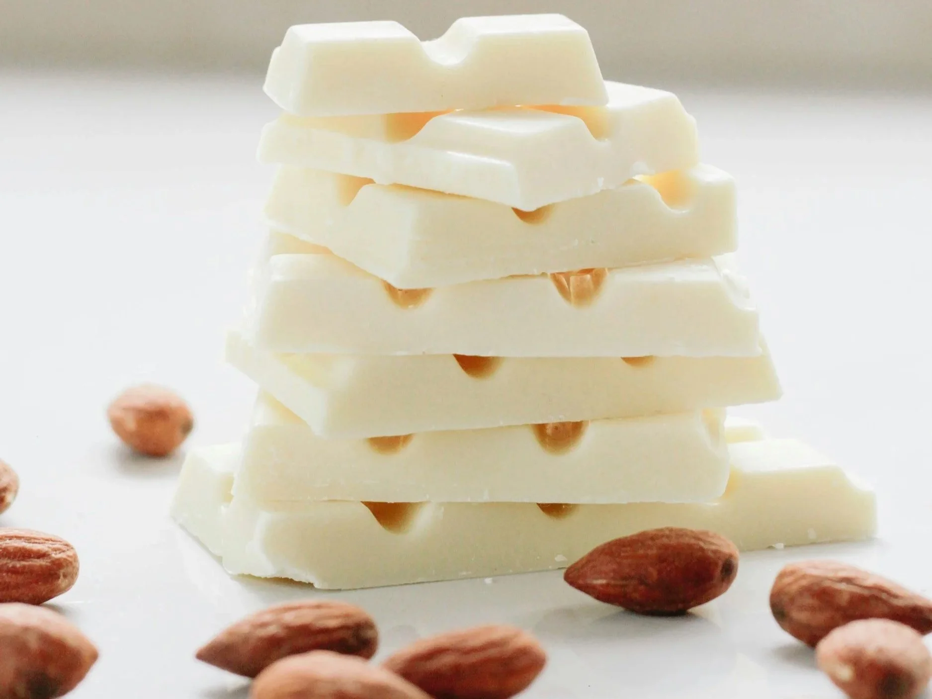 A small stack of hopped white chocolate provides the focal point for this image, with scattered almonds in the foreground.