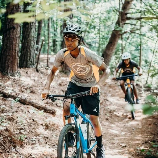 Two children riding mountain bikes on a dirt trail in a forest, wearing helmets for safety.