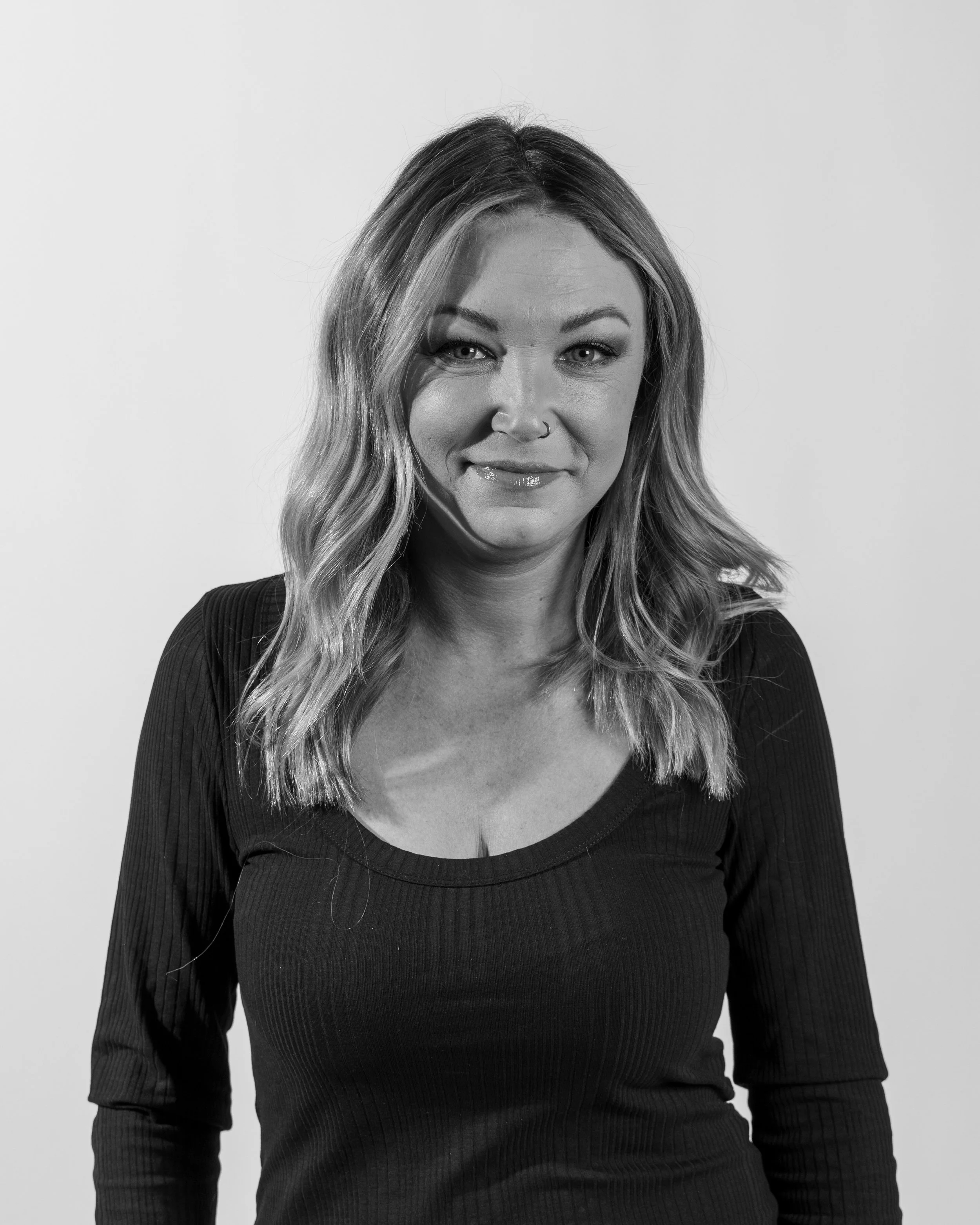 Black and white portrait of a smiling woman with wavy hair, wearing a long-sleeve top, against a plain background.