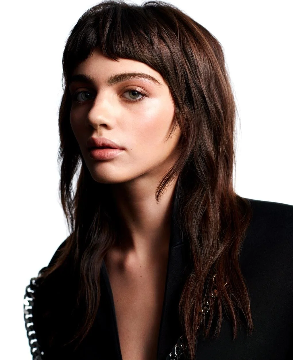 A portrait of a young woman with long brown hair, light makeup, and a black top, looking at the camera against a white background.