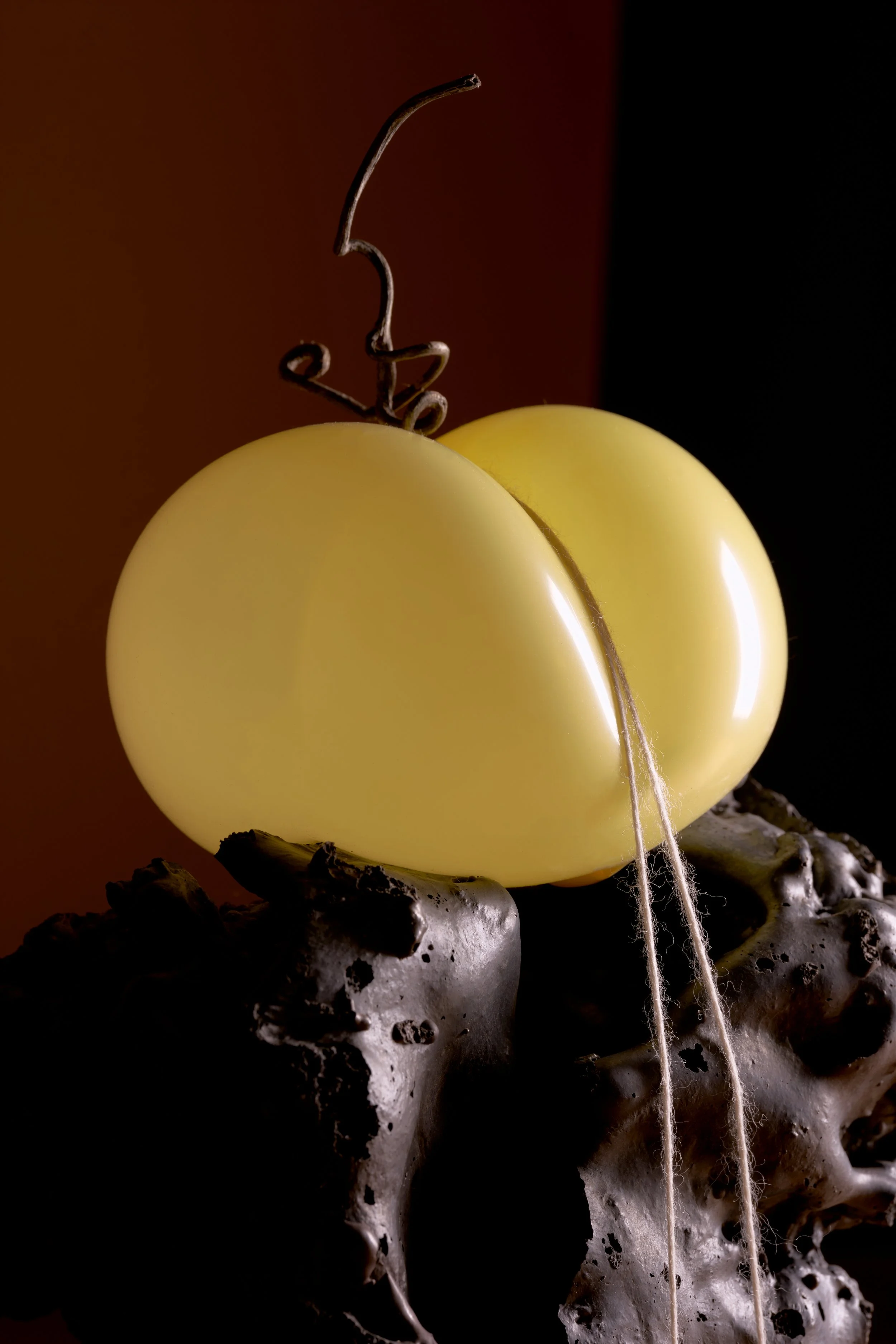 A decorative object resembling a cherry made of yellow eggs with a metal wire stem, placed on a textured dark base, with a dark and warm background.