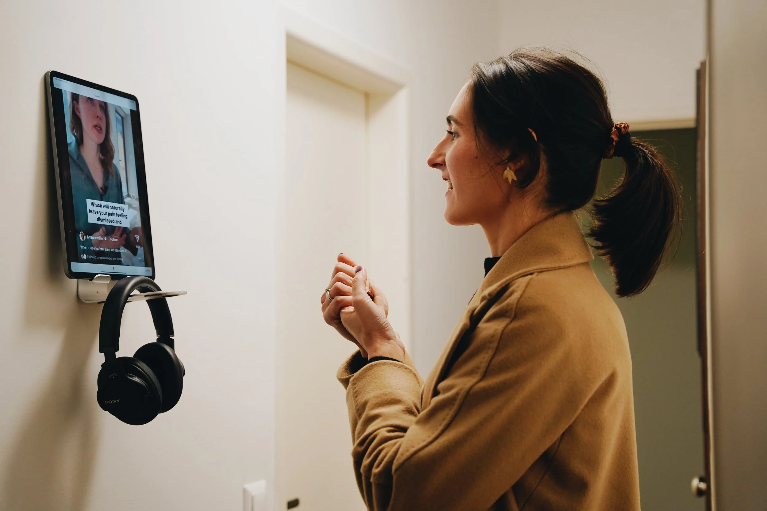 Woman watching a video on a mounted tablet with earphones hanging on the wall beside her.