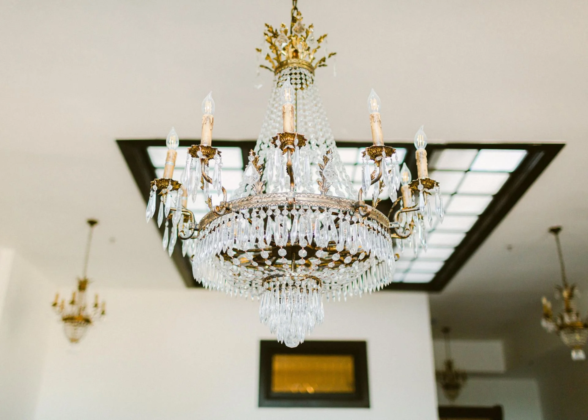 Elegant chandelier with multiple crystal prisms hanging from a gold frame in a well-lit room.