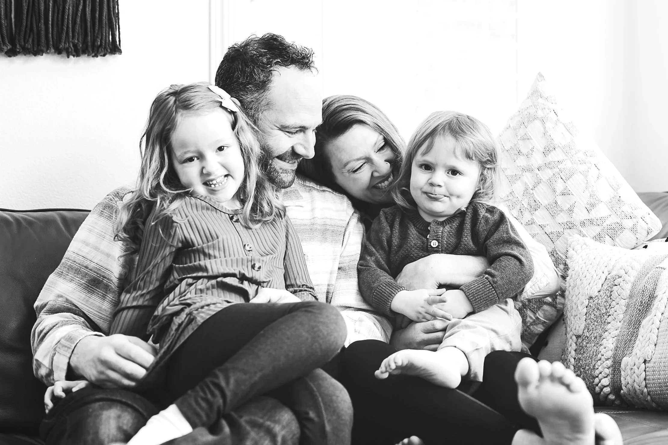 A family of 4, including a man, woman, and young girl, enjoying time outdoors with the man and woman holding the girl and all smiling happily.