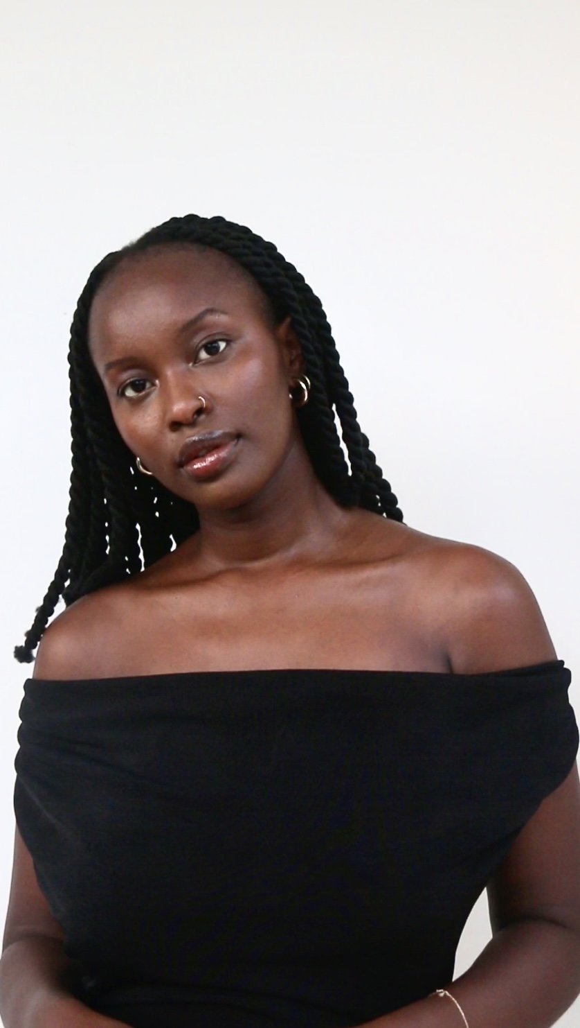 A smiling woman with dreadlocks, wearing large sunglasses and a colorful tie-dye shirt.