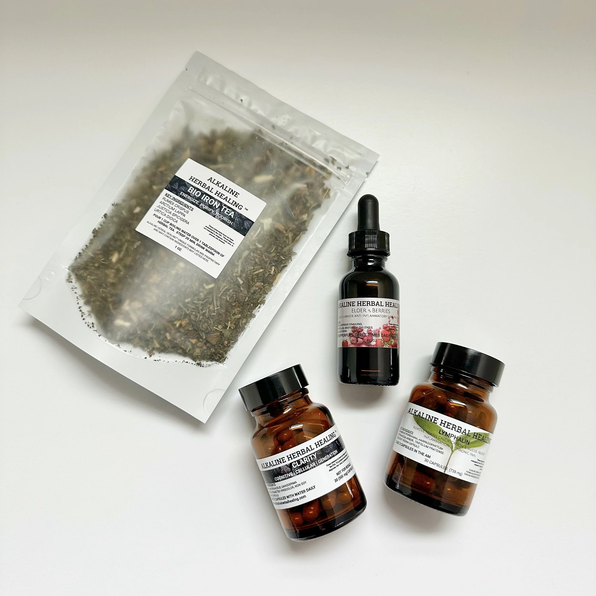 Three Bottles of Alkaline Herbal Health Supplements and a bag of herbal tea on a white surface.