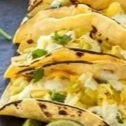 Three tacos filled with lettuce, cheese, and grilled chicken, garnished with cilantro