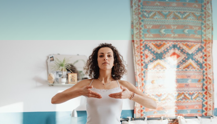 Woman in a white tank top with curly hair practicing yoga or meditation indoors.