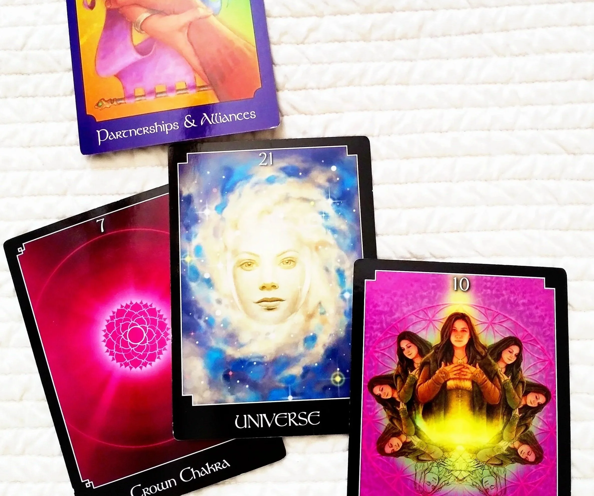 Tarot cards featuring spiritual and mystical themes, including a card with a human face and cosmic background, and other cards with symbols and women with long hair, laid on a white textured surface.
