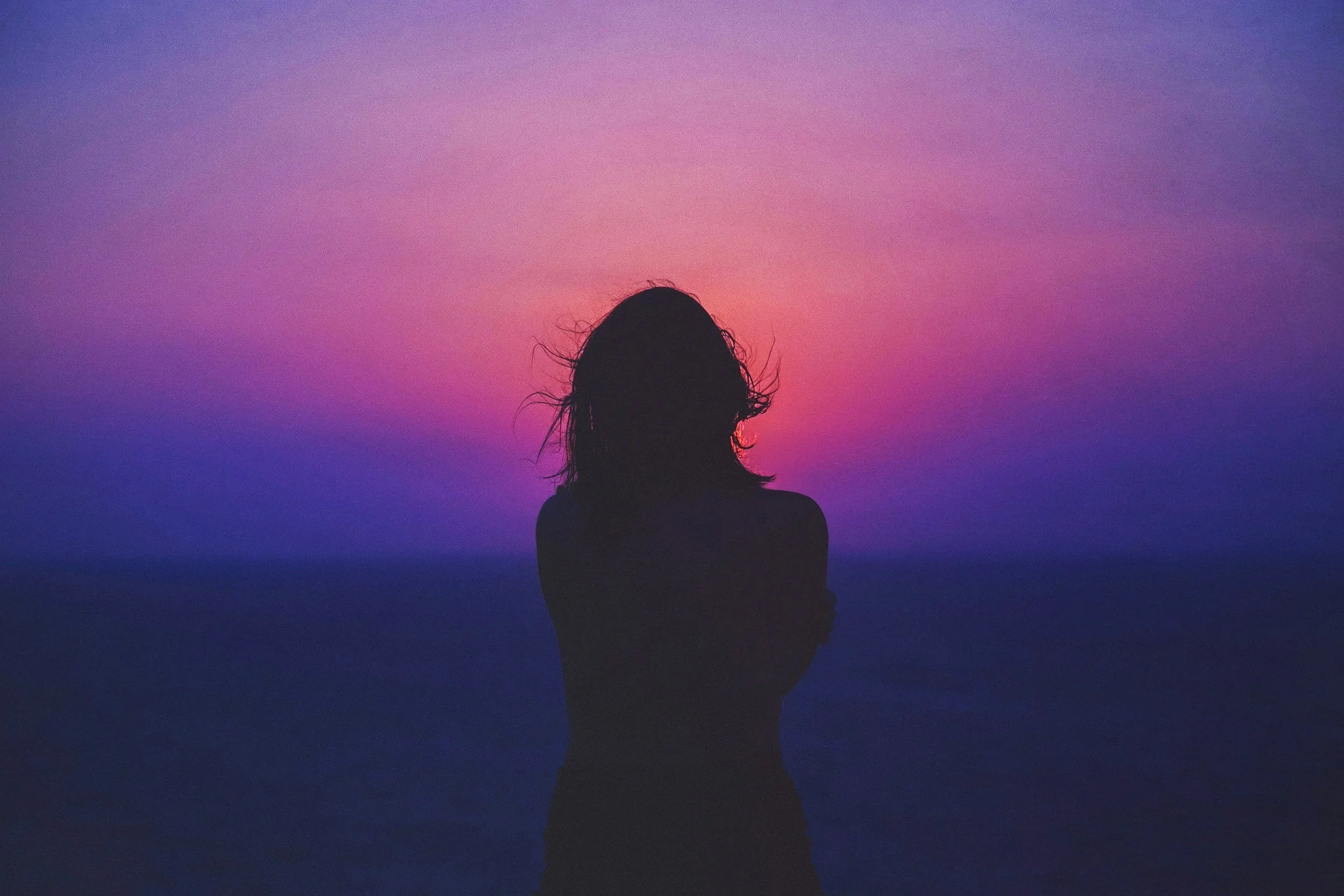 Silhouette of a person with wet hair against a purple and pink sunset sky.