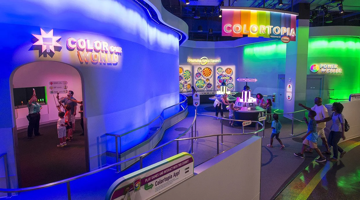Interior of an interactive exhibit called Colortopia, featuring colorful displays, LED lights, and visitors, including children, exploring different color-related activities and displays.