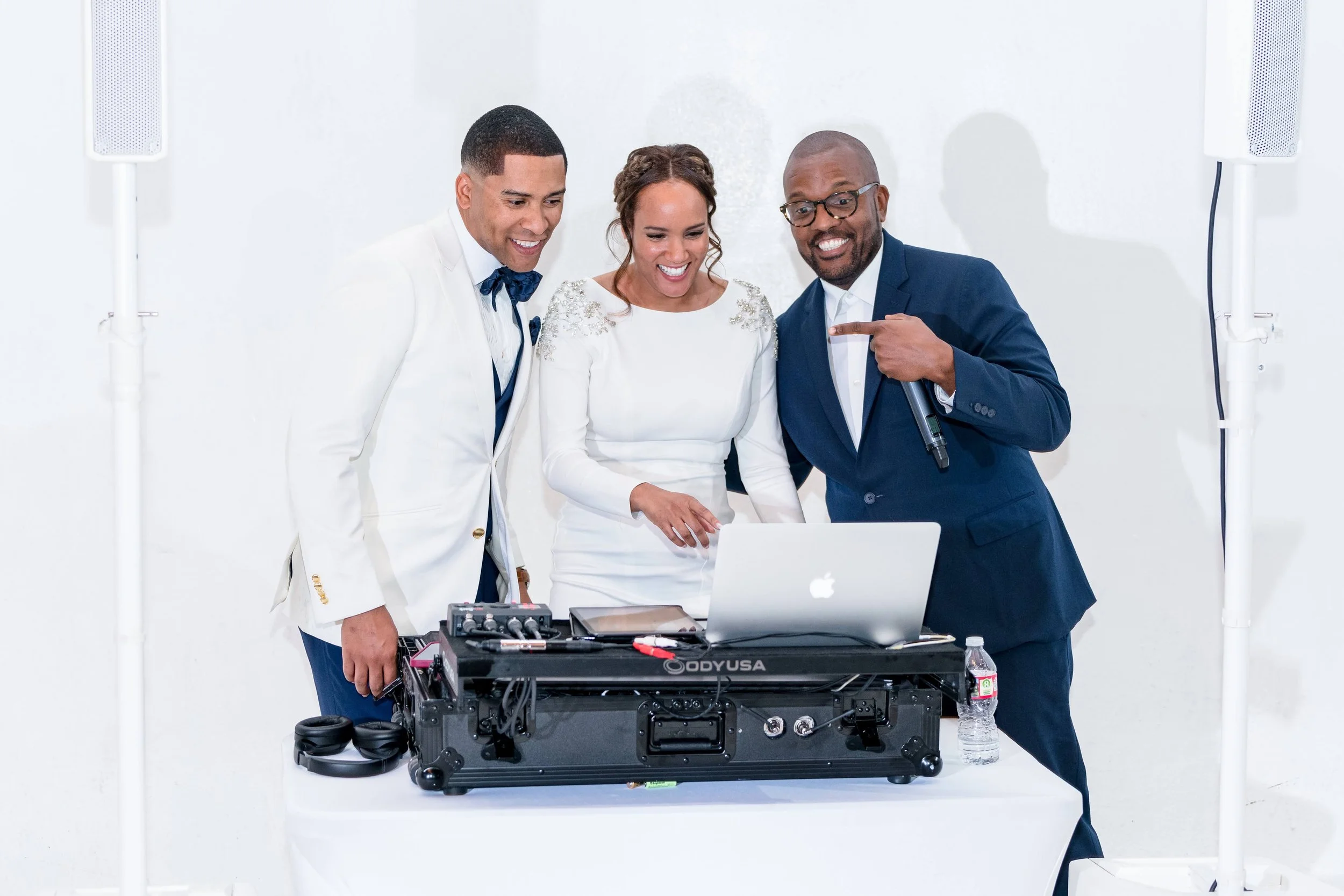Three people smiling behind a DJ setup with a laptop and audio equipment.