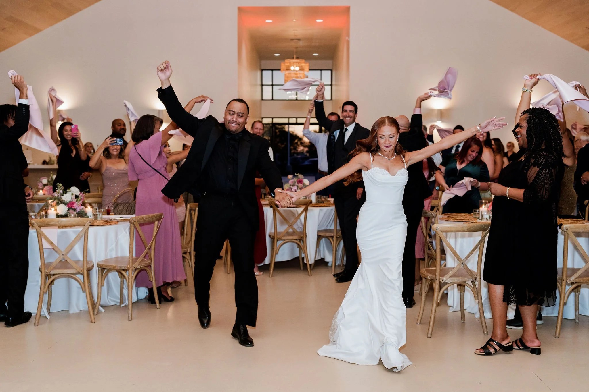 A couple dances happily at their wedding reception, surrounded by cheering guests.