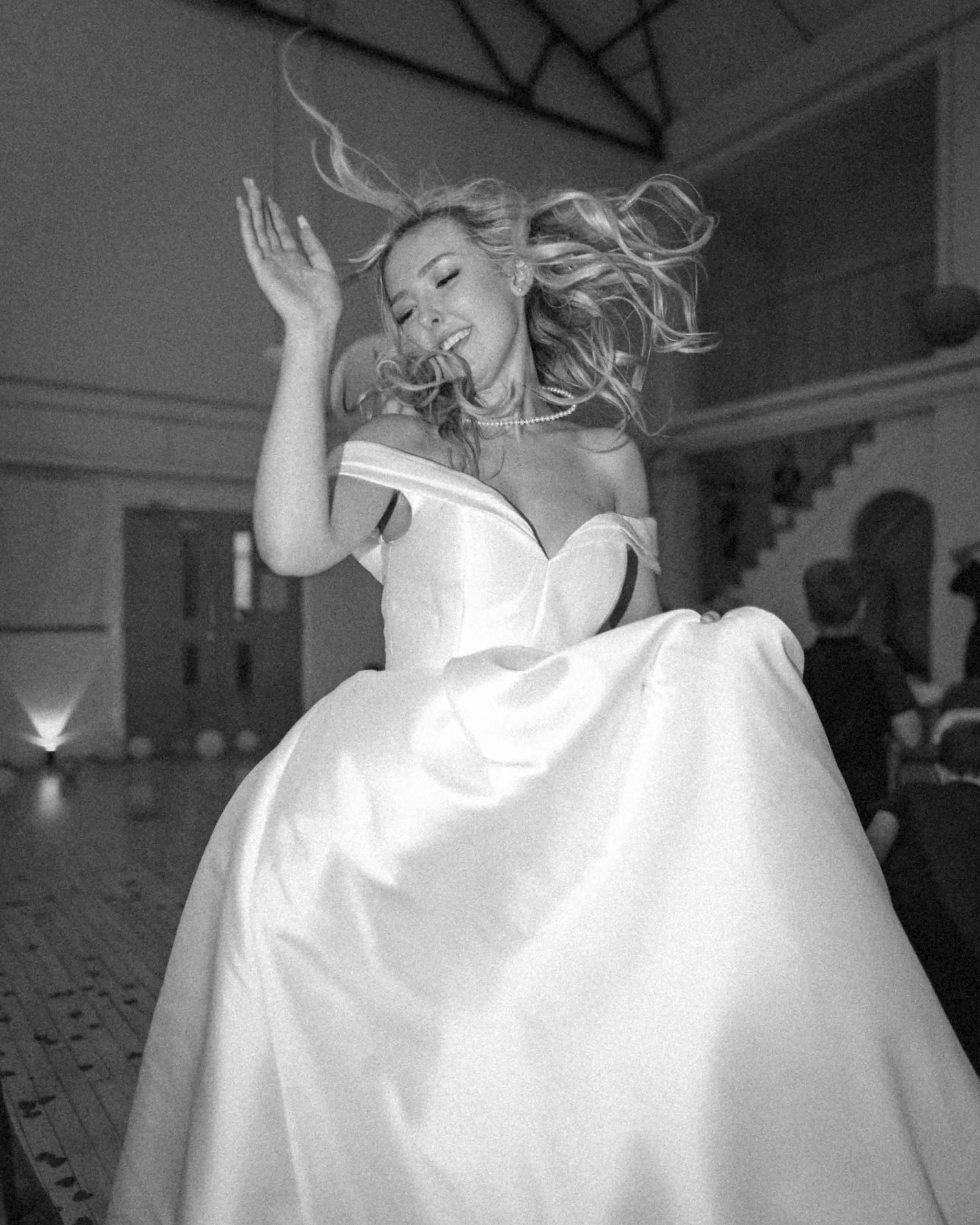 Black and white photo of a woman dancing in a flowing gown, with hair twirling and a joyful expression.