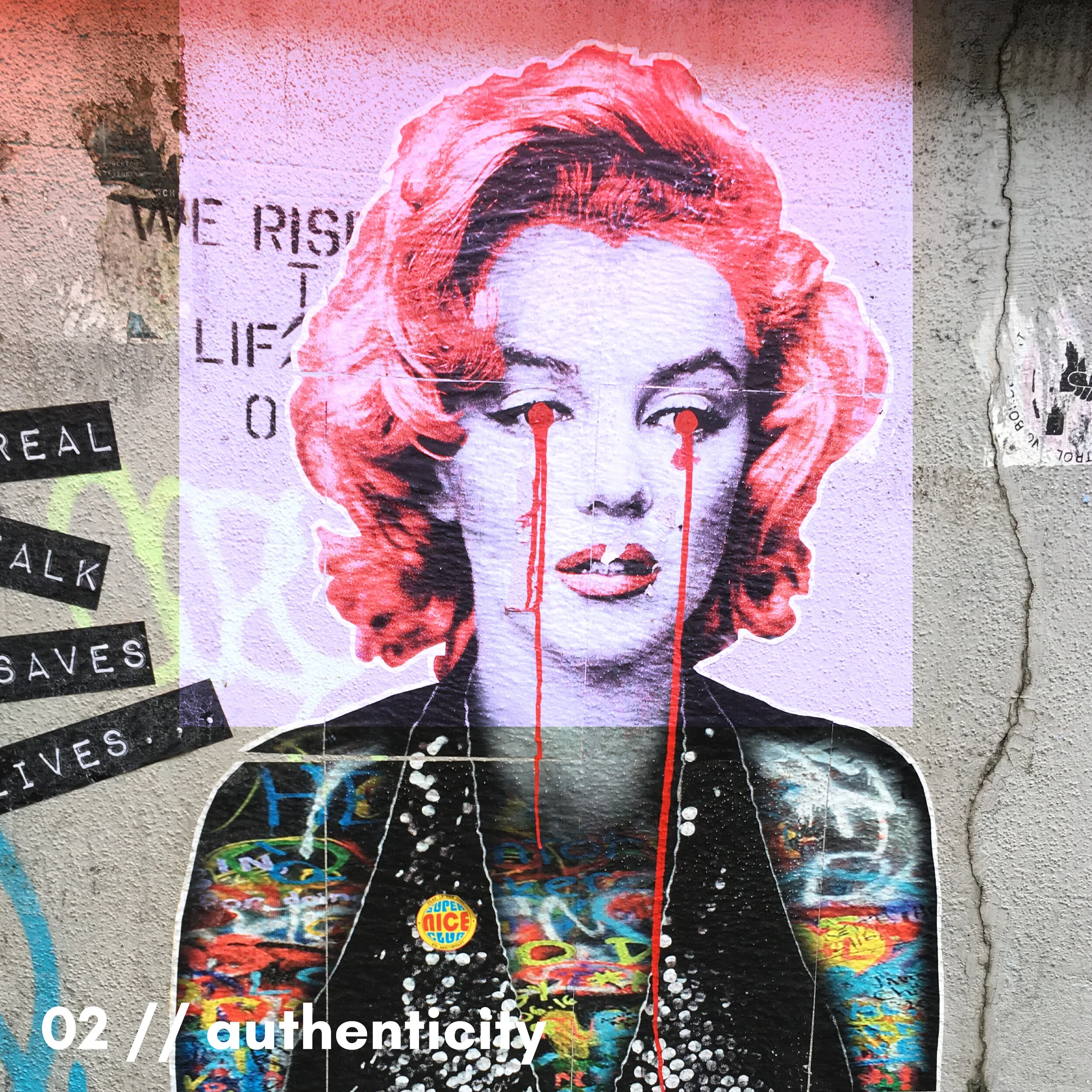 Street art mural of a woman's face with red hair, black and red facial features, and red tears, on a concrete wall with various stickers and graffiti around.