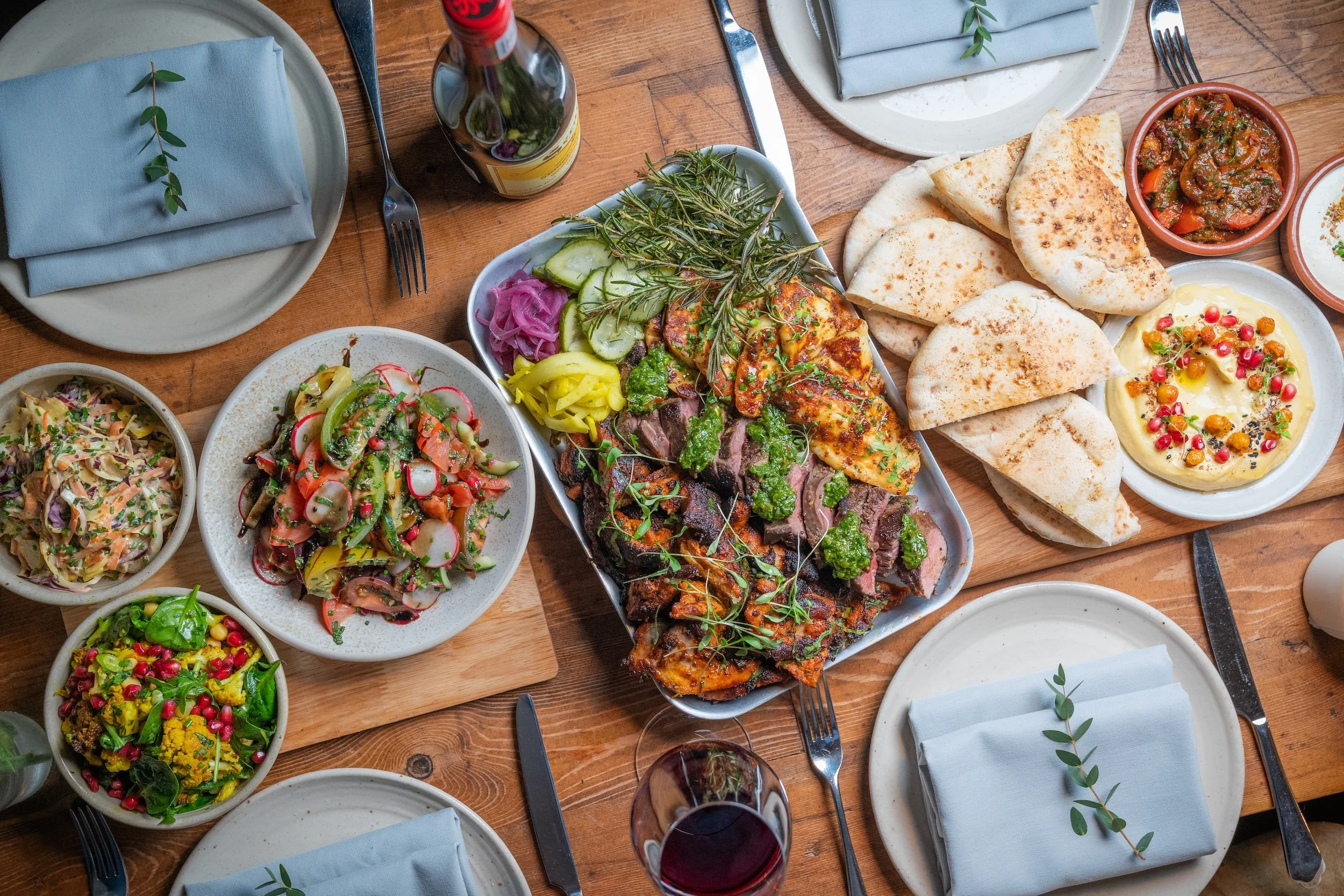 A picture of FEDs Private Catering Feast Buffet including various dishes including grilled vegetables, salads, dips, bread, and appetizers on a table decorated with flowers.