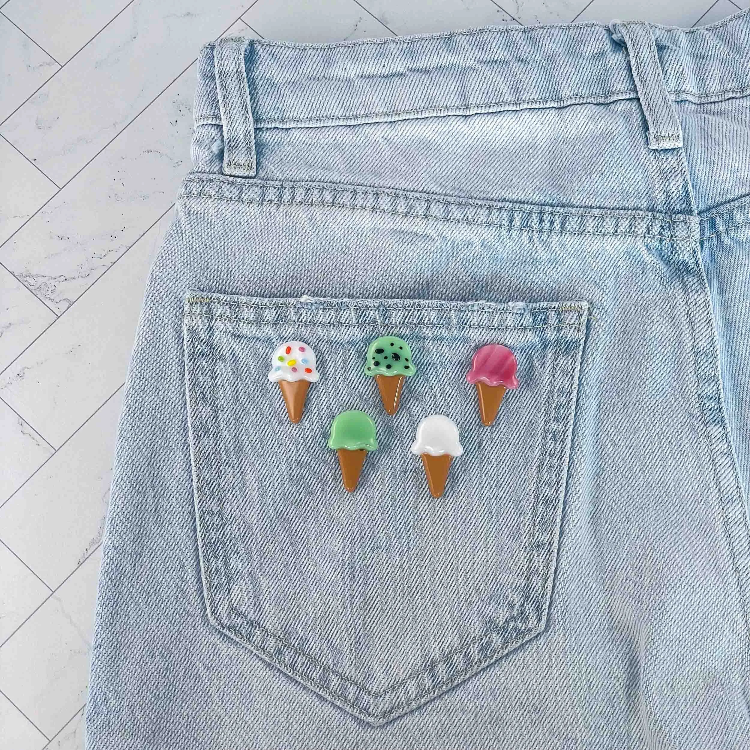 Various colored fused glass ice cream cone pins attached to the back pocket of a pair of blue jeans