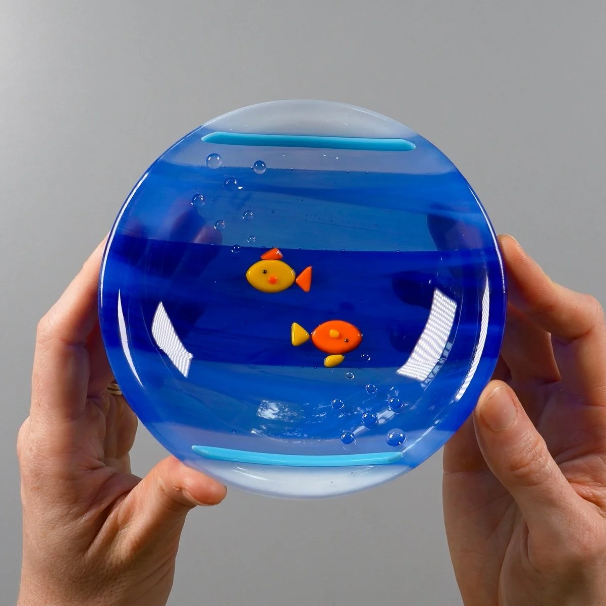 Hands holding a finished fused glass 'Fish Bowl' dish