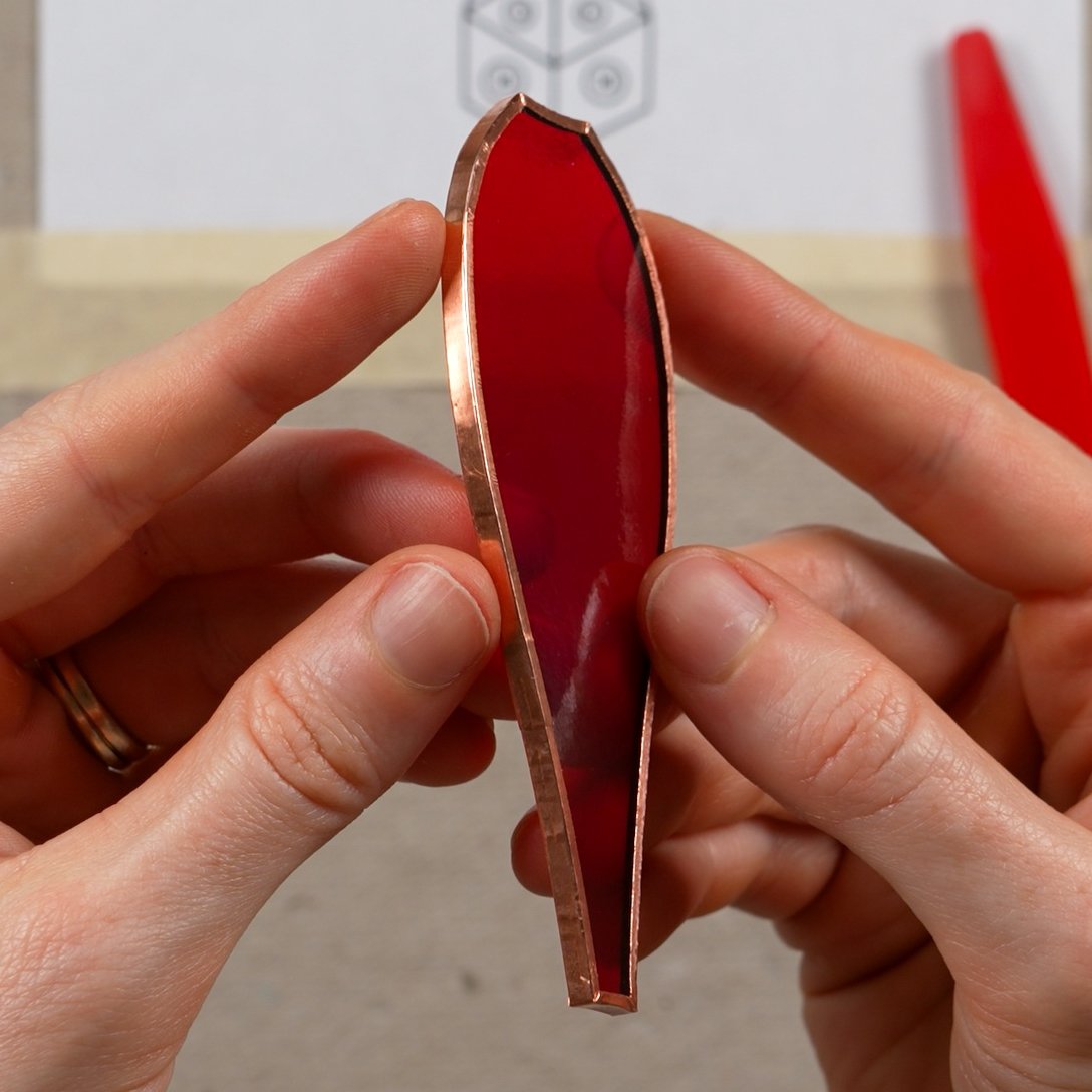 A red stained glass shape wrapped and smoothly burnished with copper foil