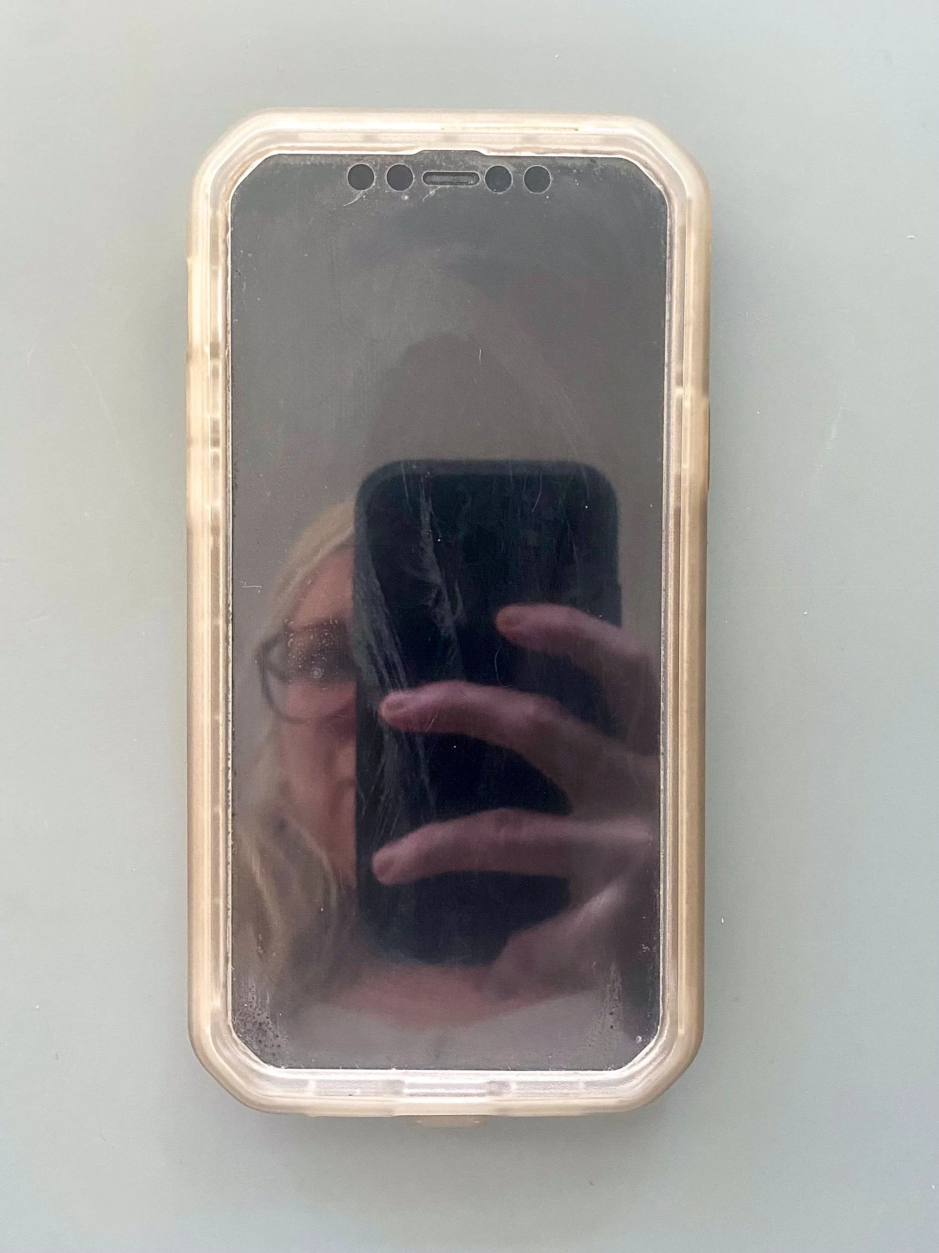 An iphone on a table, with its black screen reflecting Jackie Knowles of Glasswork Pixie photographing it using another iphone