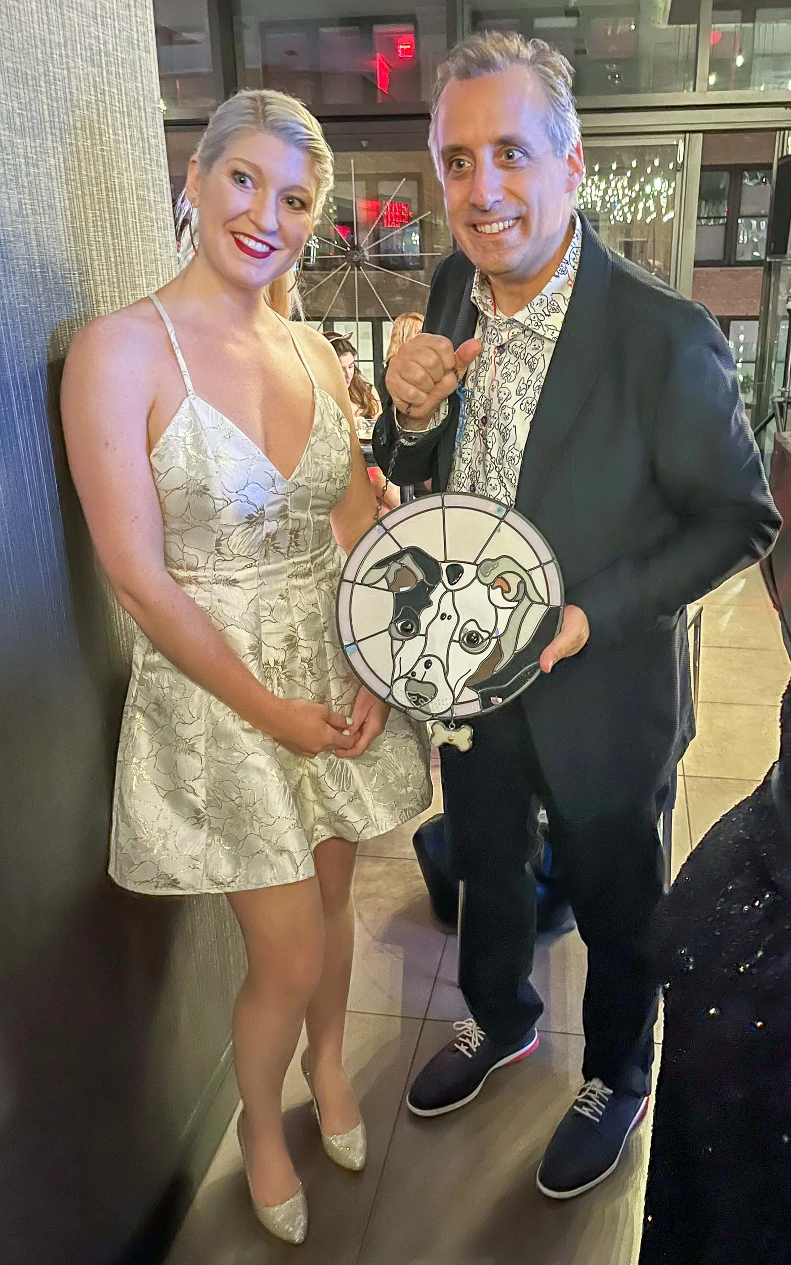 Jackie Knowles of Glasswork Pixie next to Joe Gatto of Impractical Jokers, with Joe holding a stained glass pet portrait of his dog that Jackie made