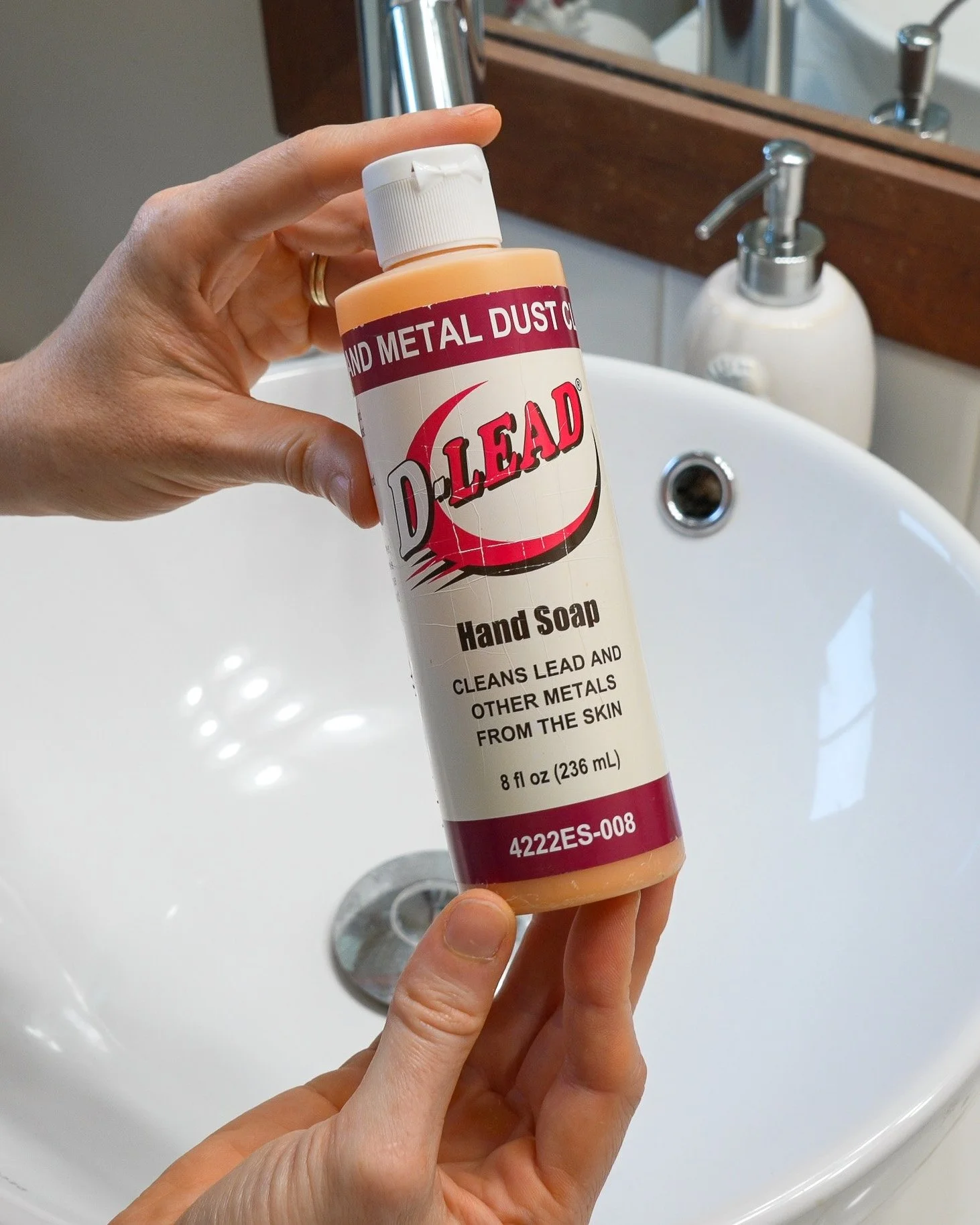 Hands holding a bottle of de-leading hand soap above a bathroom sink